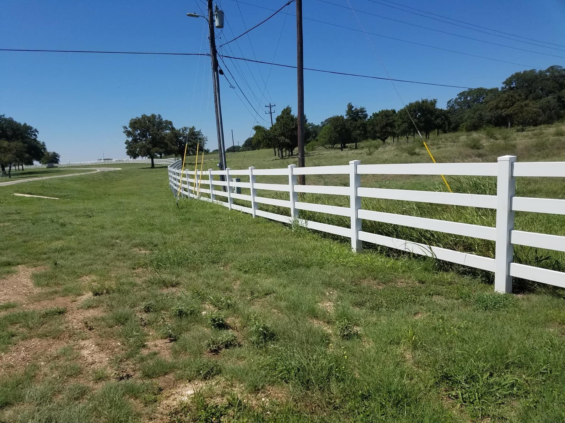 White four-rail ranch fence running across a green pasture