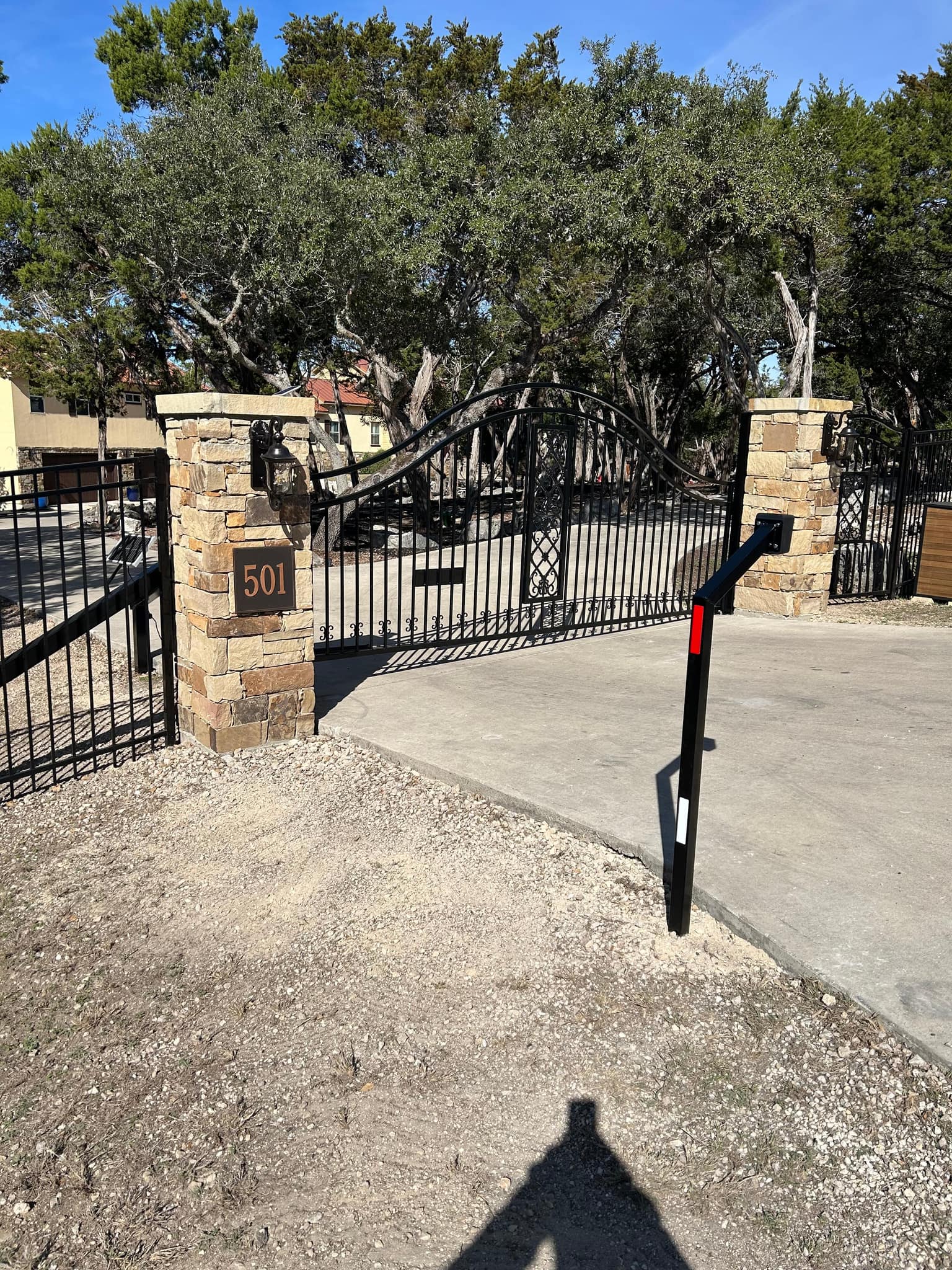 Arched black iron driveway gate with scrollwork, hung between stone columns with lanterns
