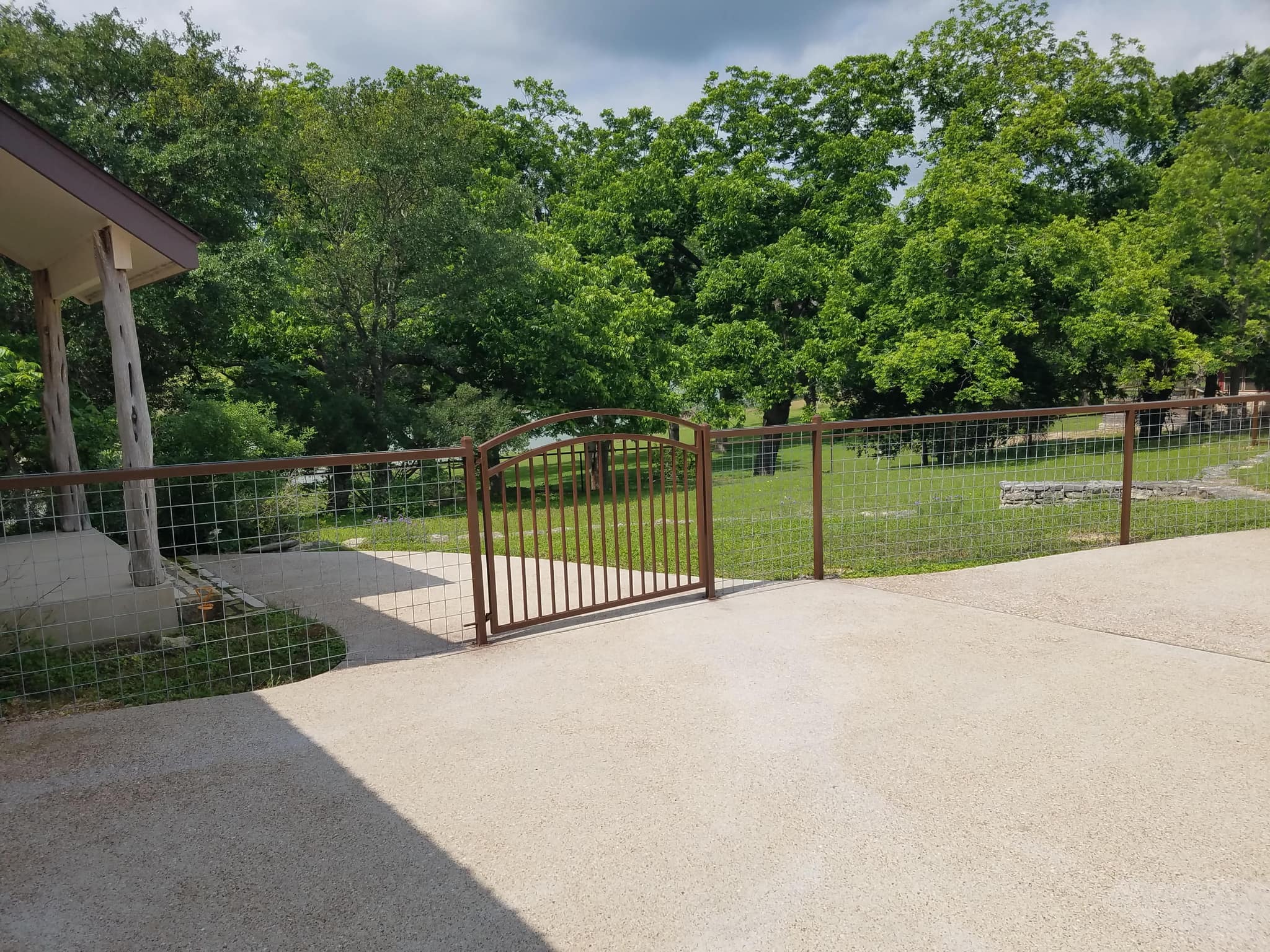 Arched brown iron driveway gate in a matching wire panel fence