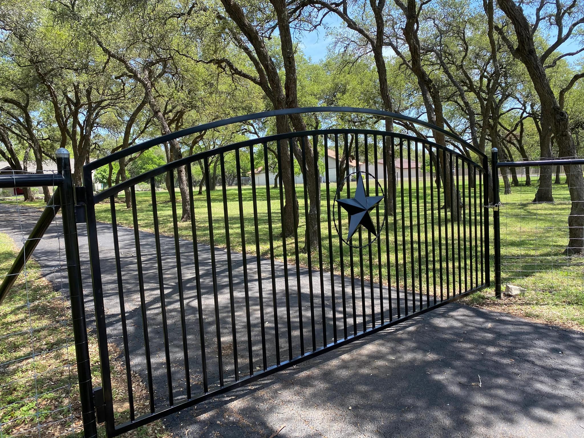 Arched black iron driveway gate with a Texas star