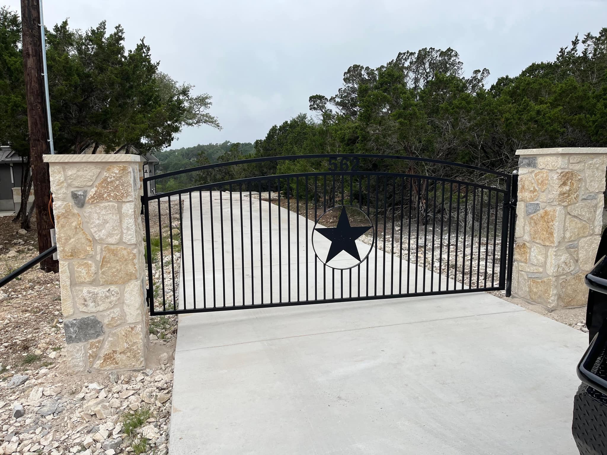 Arched iron gate with a large star between stone columns across a concrete drive