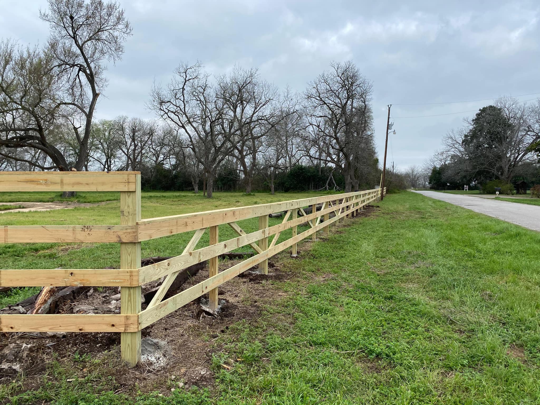 New three-rail wood fence with X-braced panels along a road