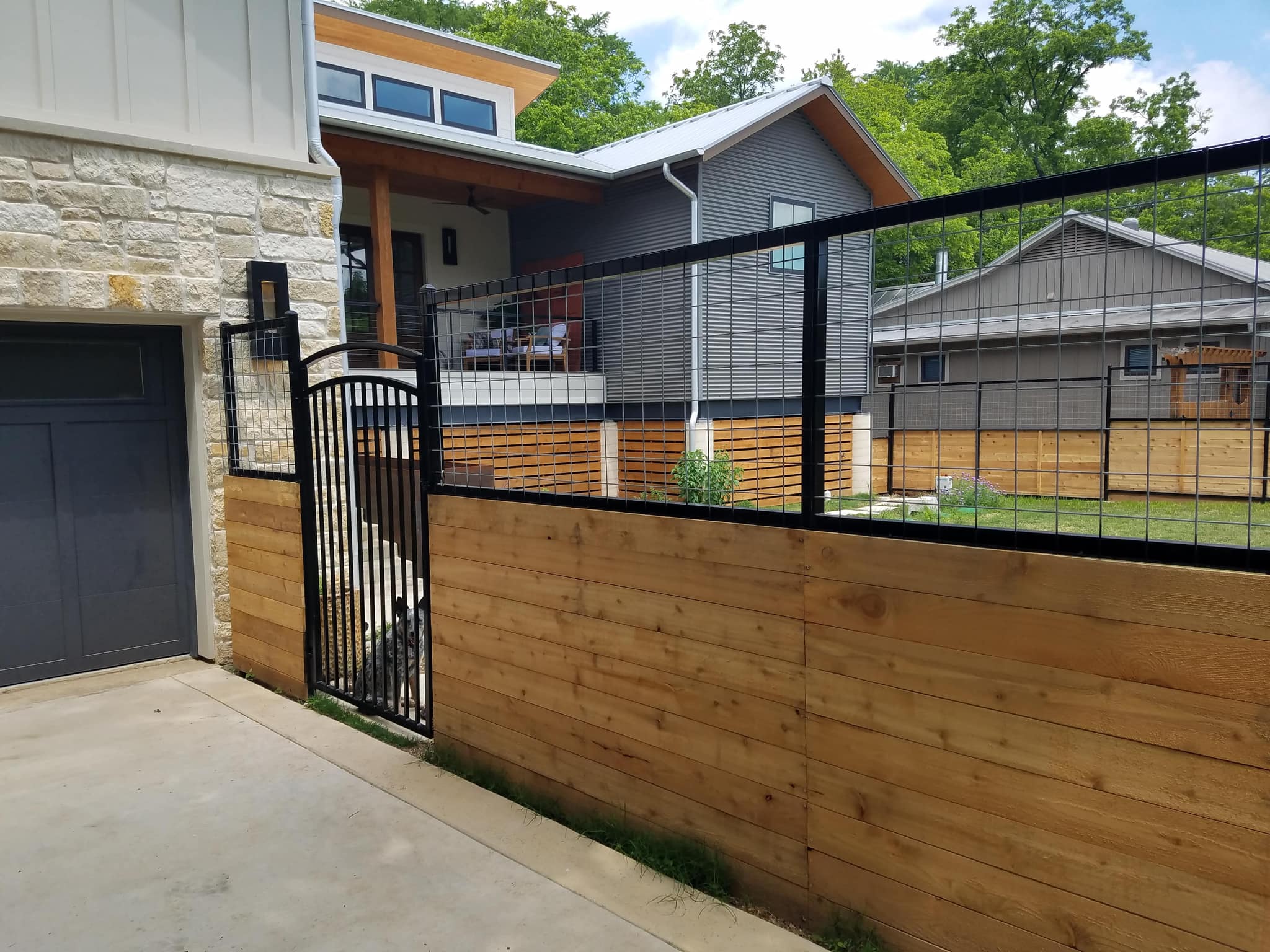 The same cedar and wire fence beside the garage, with an arched iron walk gate