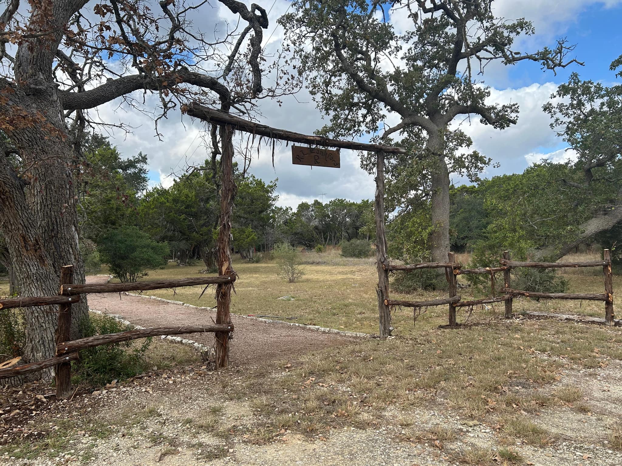 Rustic cedar entry arch with a hanging sign, joined by cedar rail fence