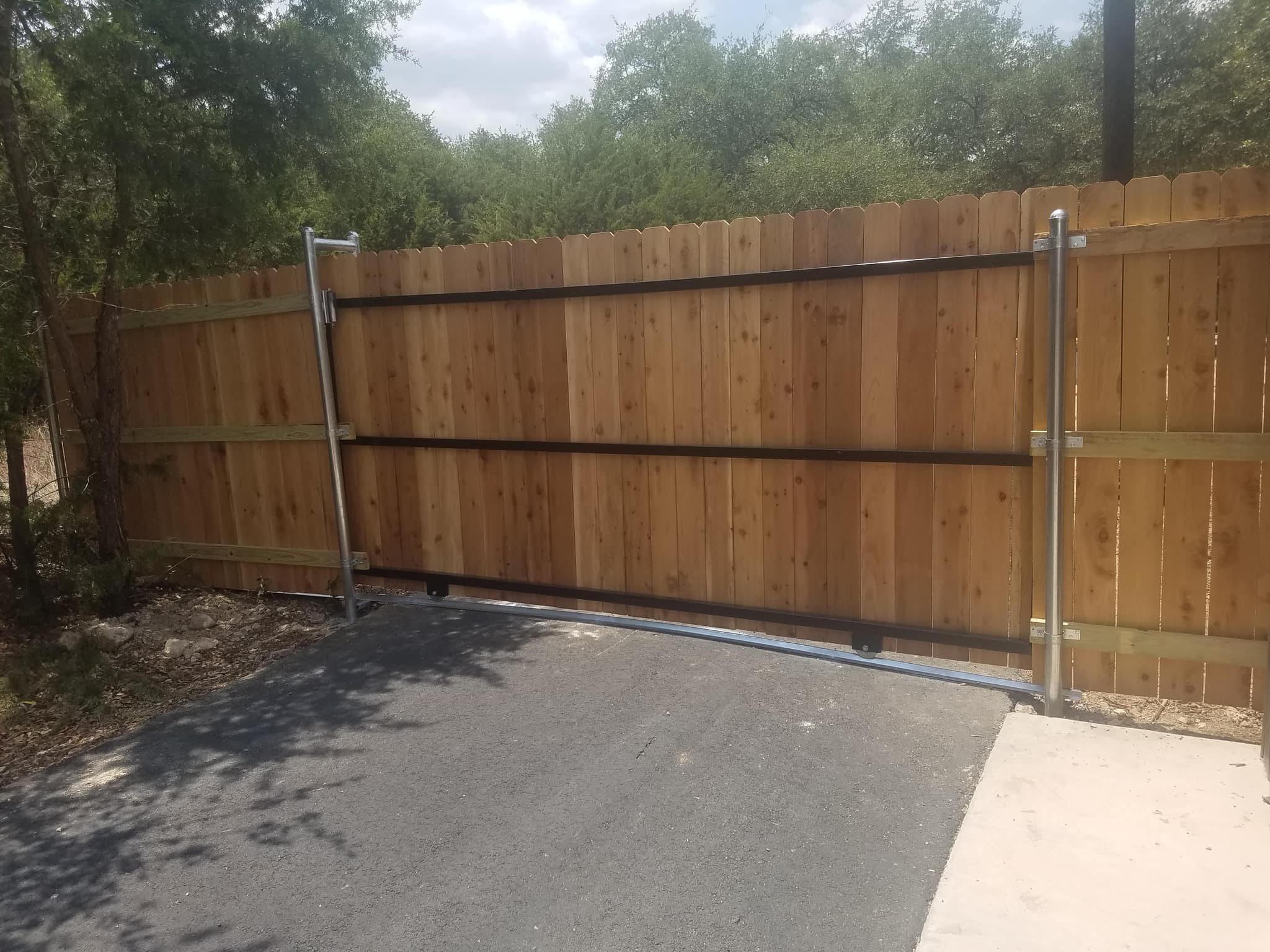 Cedar-faced steel-framed gate rolling on a track across an asphalt drive, in a cedar privacy fence