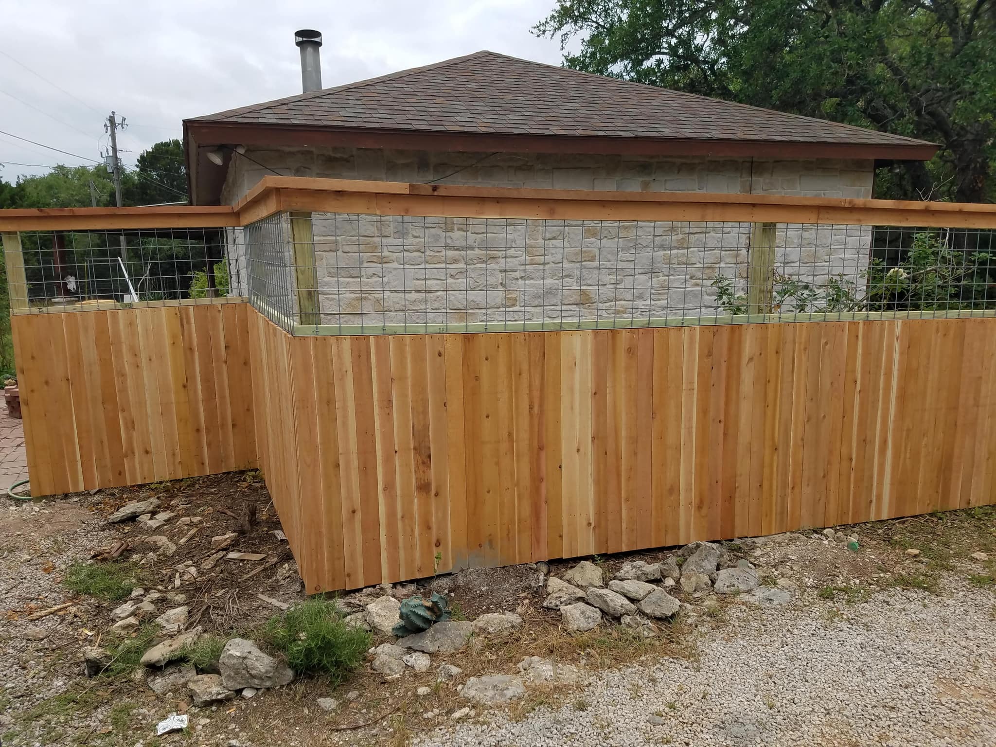 Cedar fence with welded-wire panels above it, around a stone building