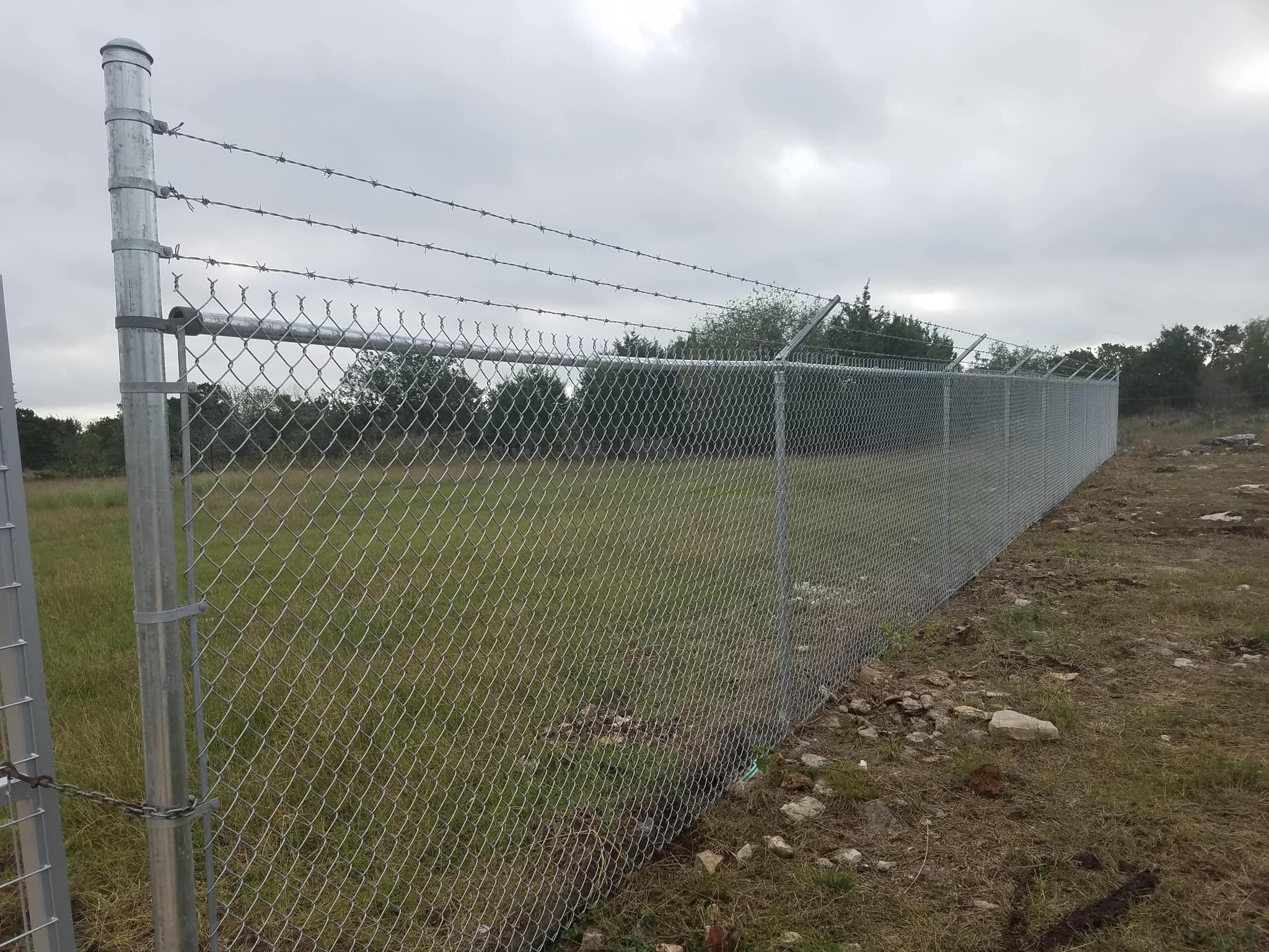 Galvanized chain link fence topped with barbed wire along open land
