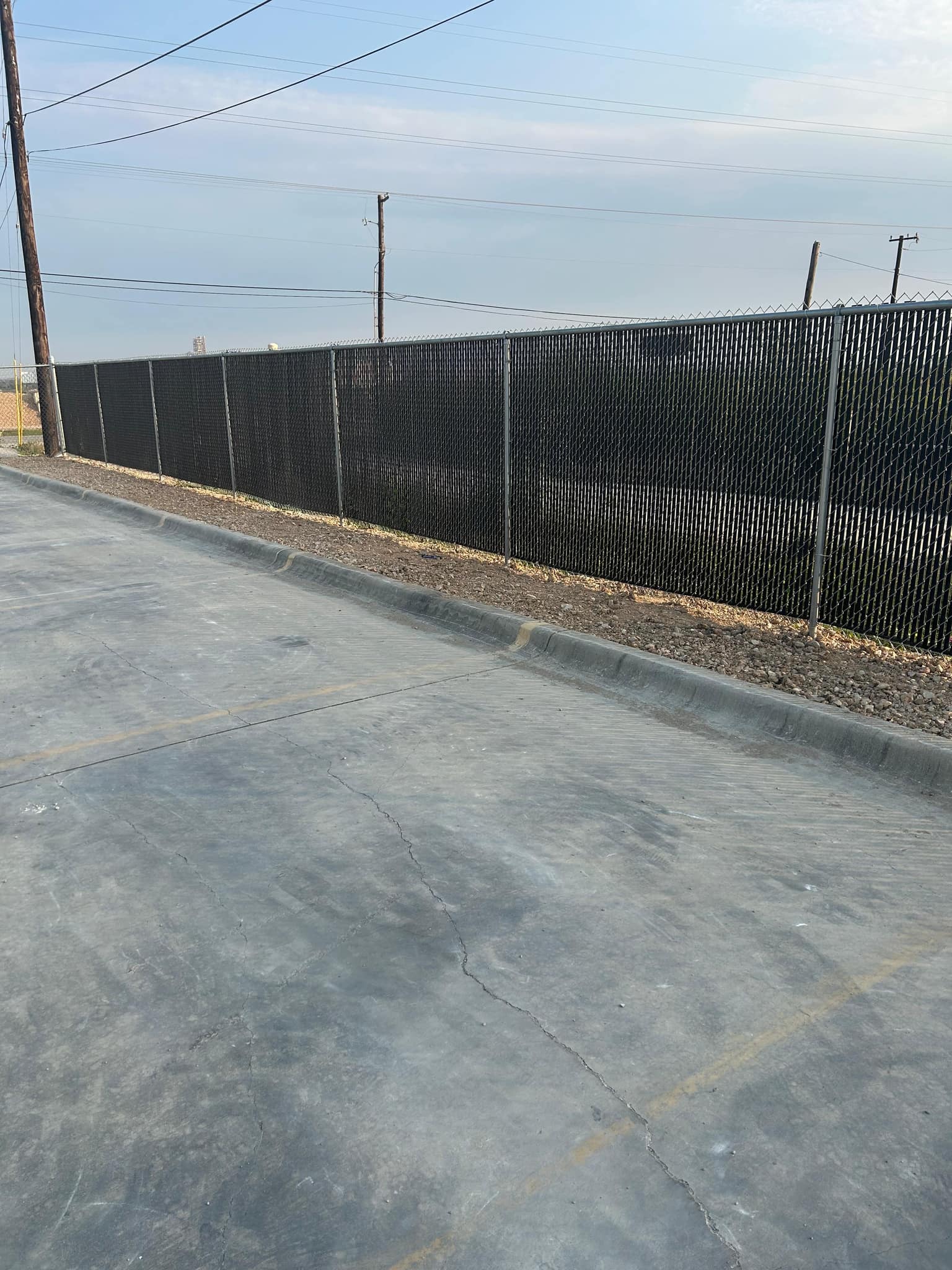 Chain link fence with black privacy slats along the edge of a paved lot