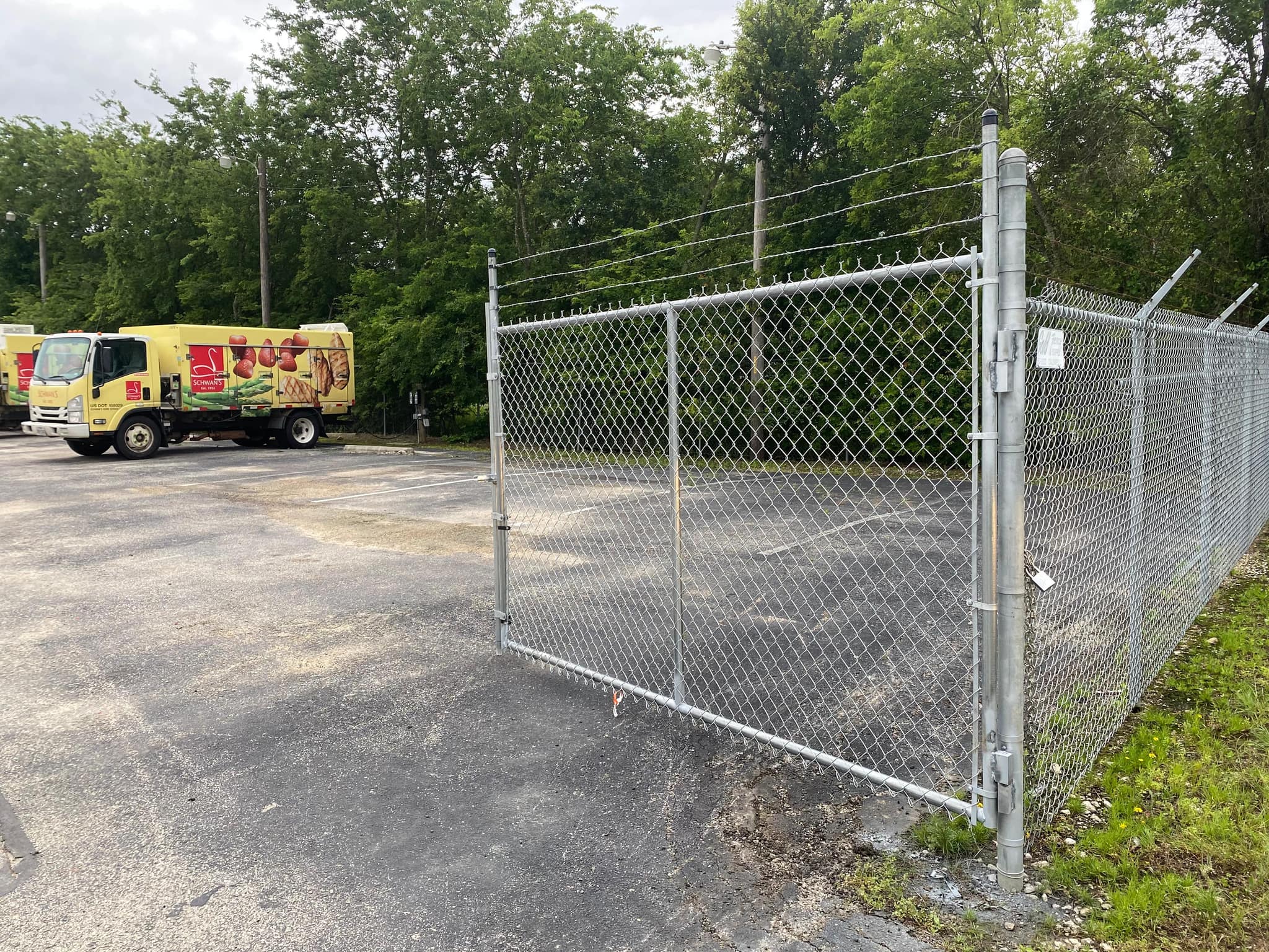 Galvanized chain link gate topped with barbed wire at a paved lot