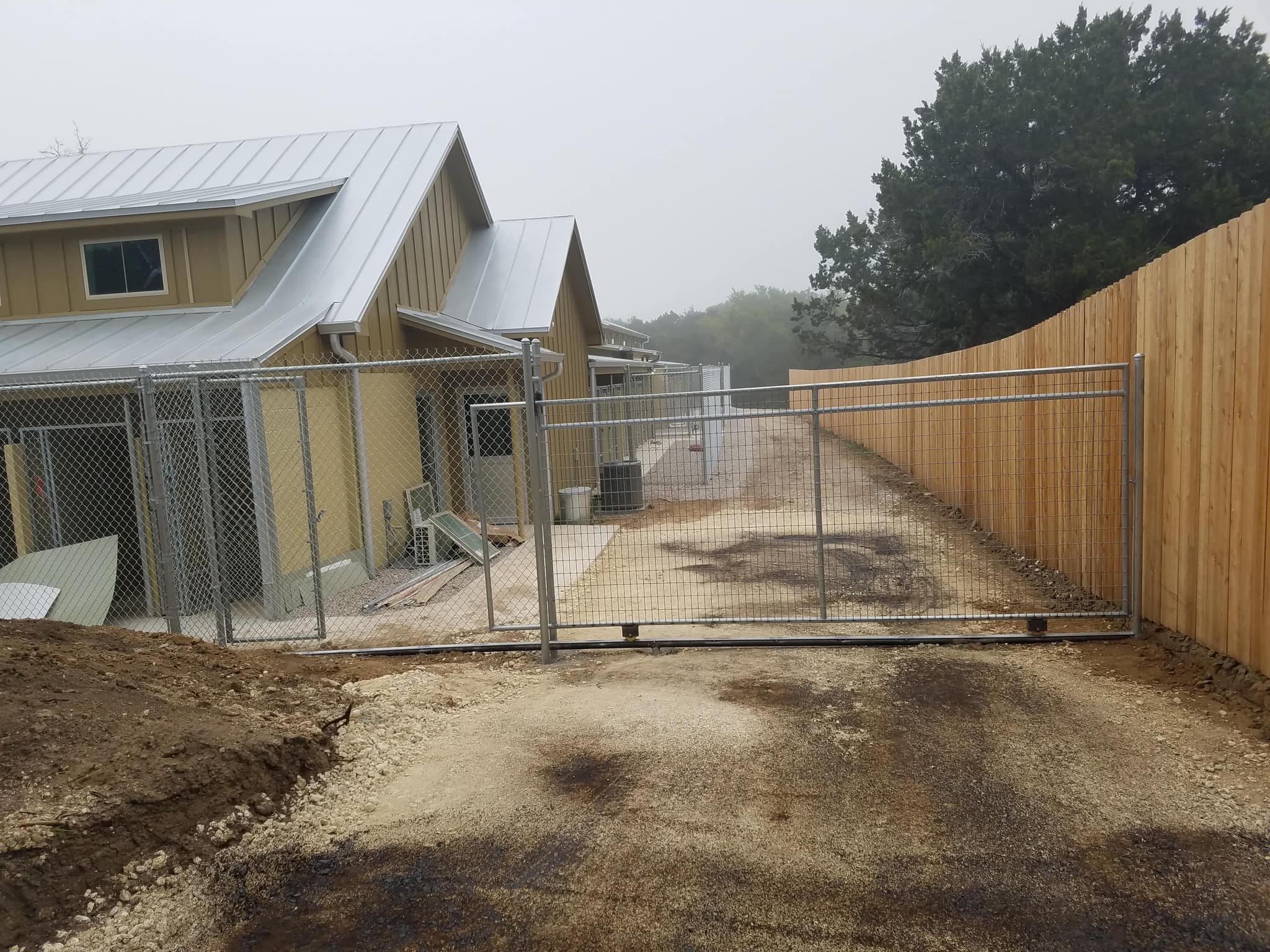 Galvanized chain link slide gate across a drive, with chain link runs along a building and a cedar privacy fence