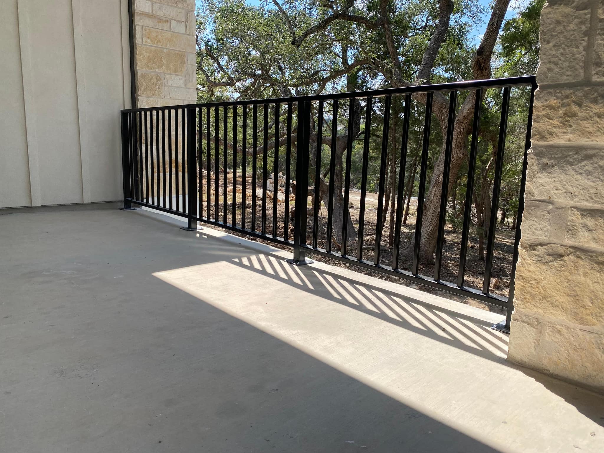 Black iron railing across a covered concrete patio, between stone columns