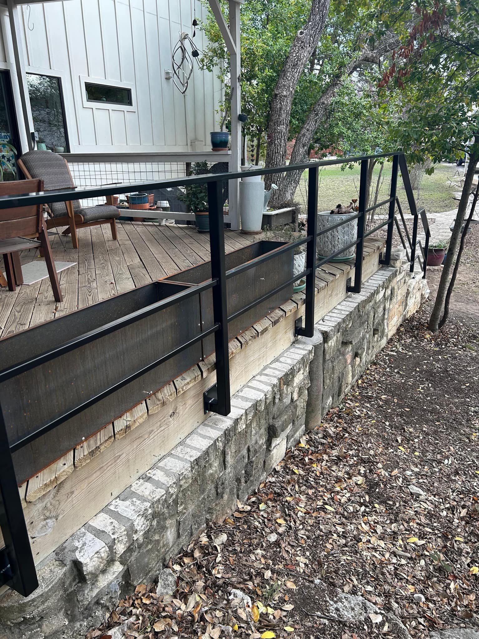 Black square-tube railing along a raised wooden deck on a stone wall