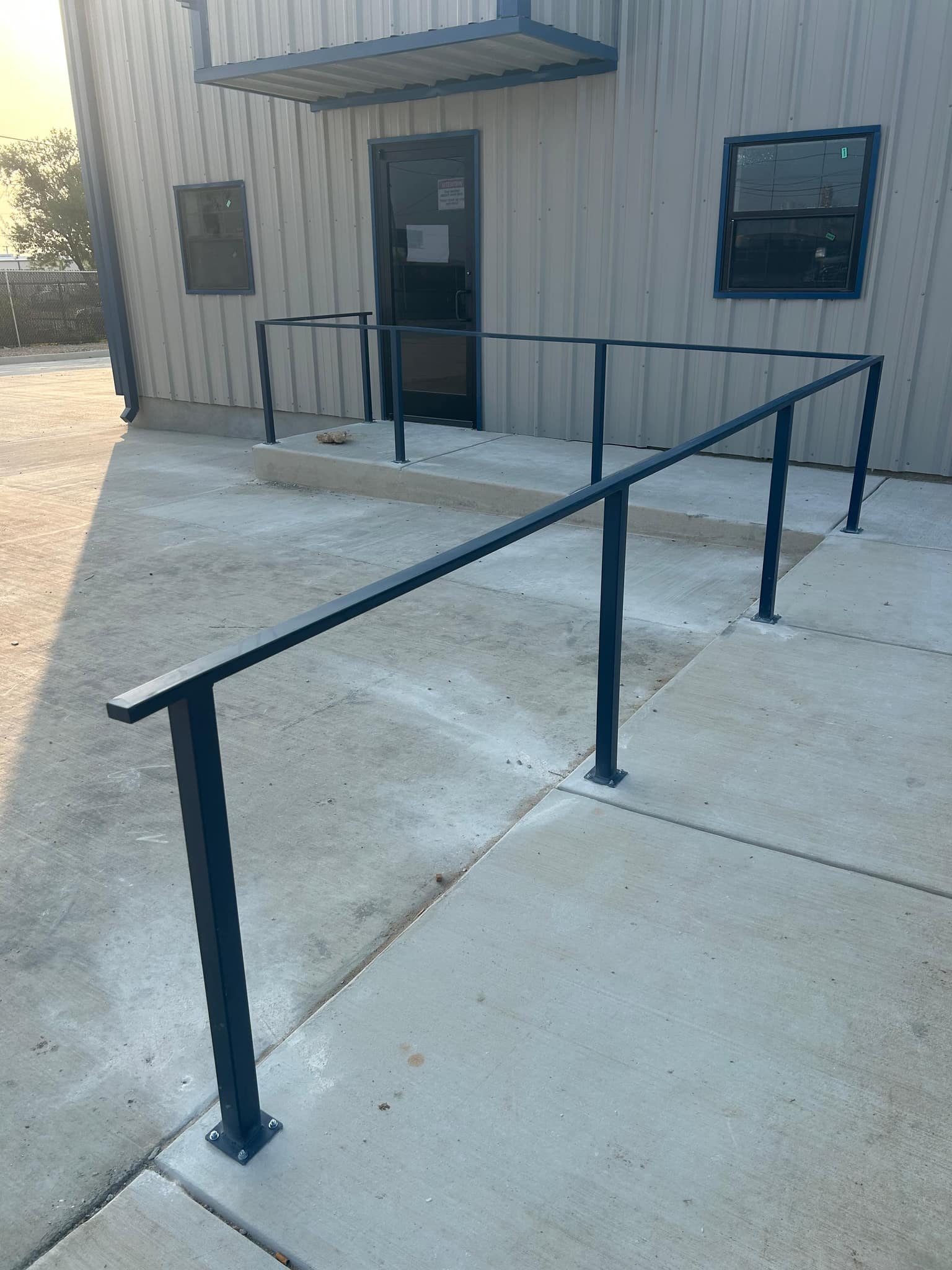 Blue steel guard rail on base plates around the entry walk of a metal building