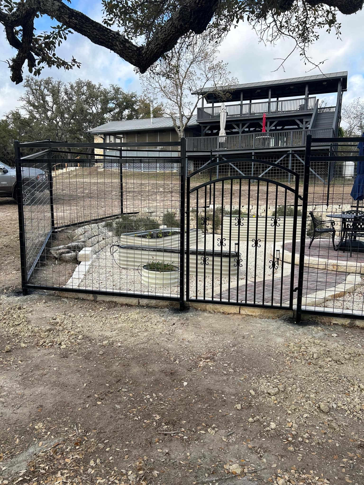 Black welded-wire panel fence with an arched iron walk gate around a garden of raised beds