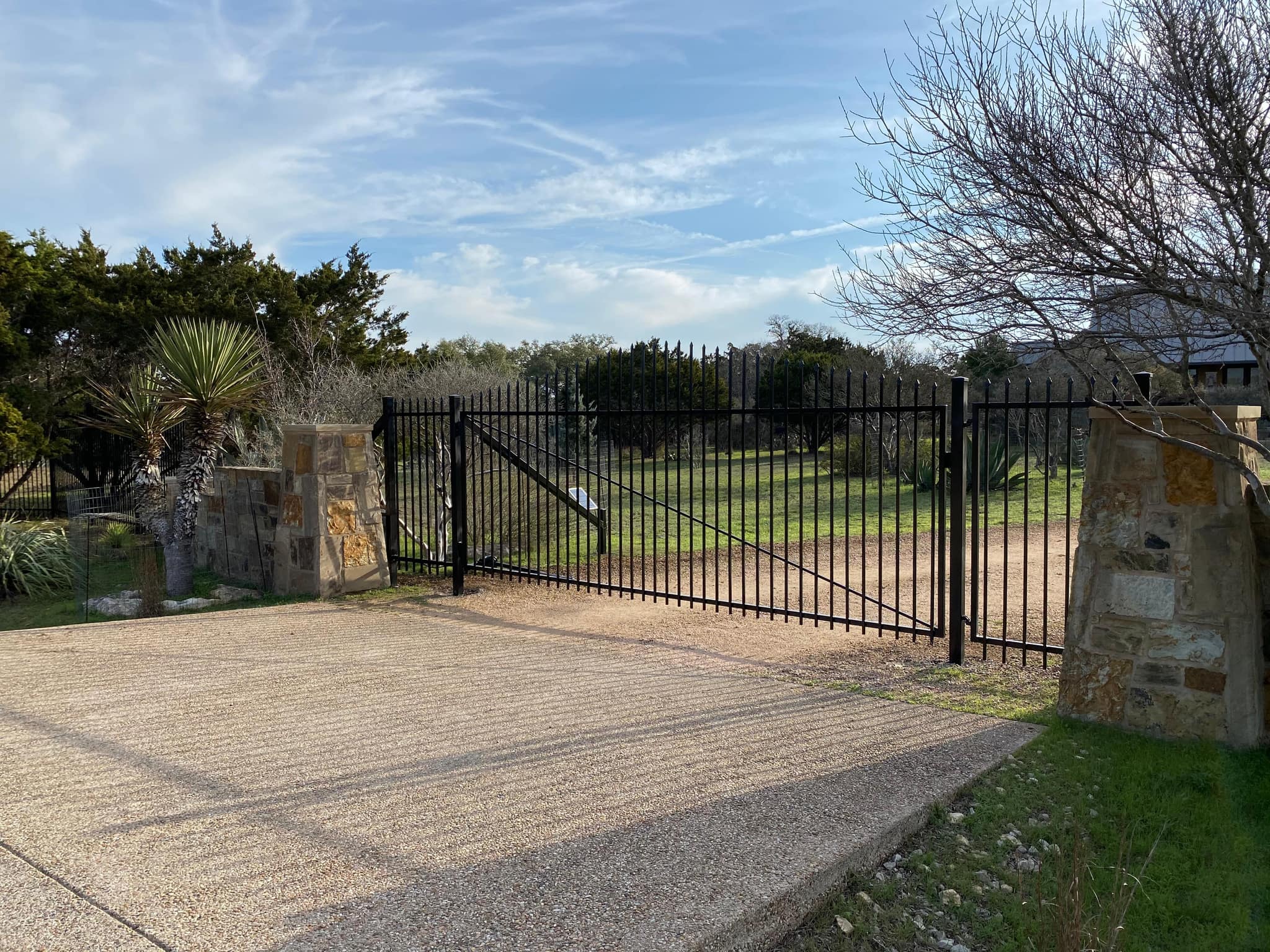 Black iron driveway gate between stone columns
