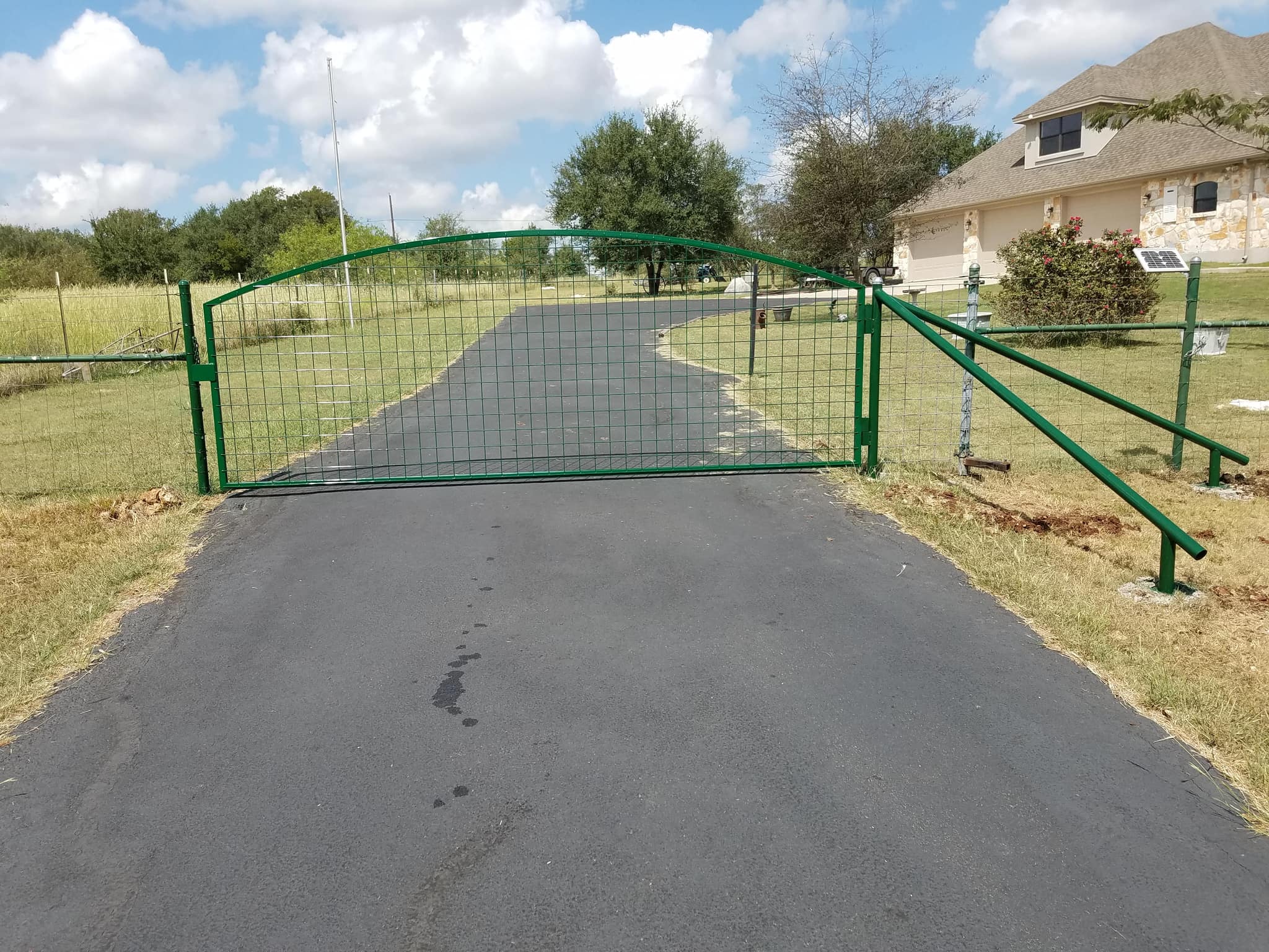 Arched green pipe gate with wire panel fill across a paved drive, with matching fence