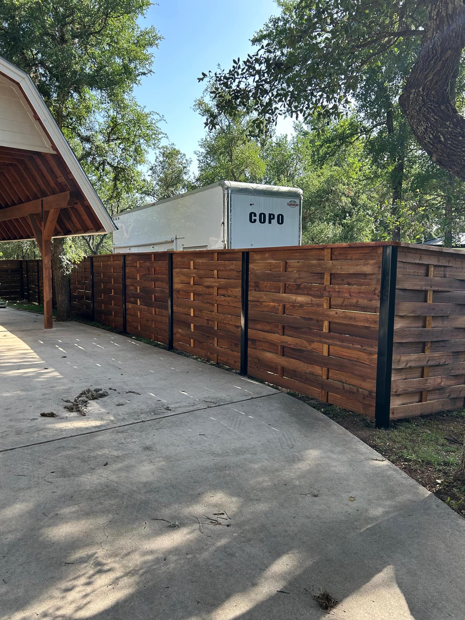 Stained horizontal cedar fence on black posts along a concrete drive