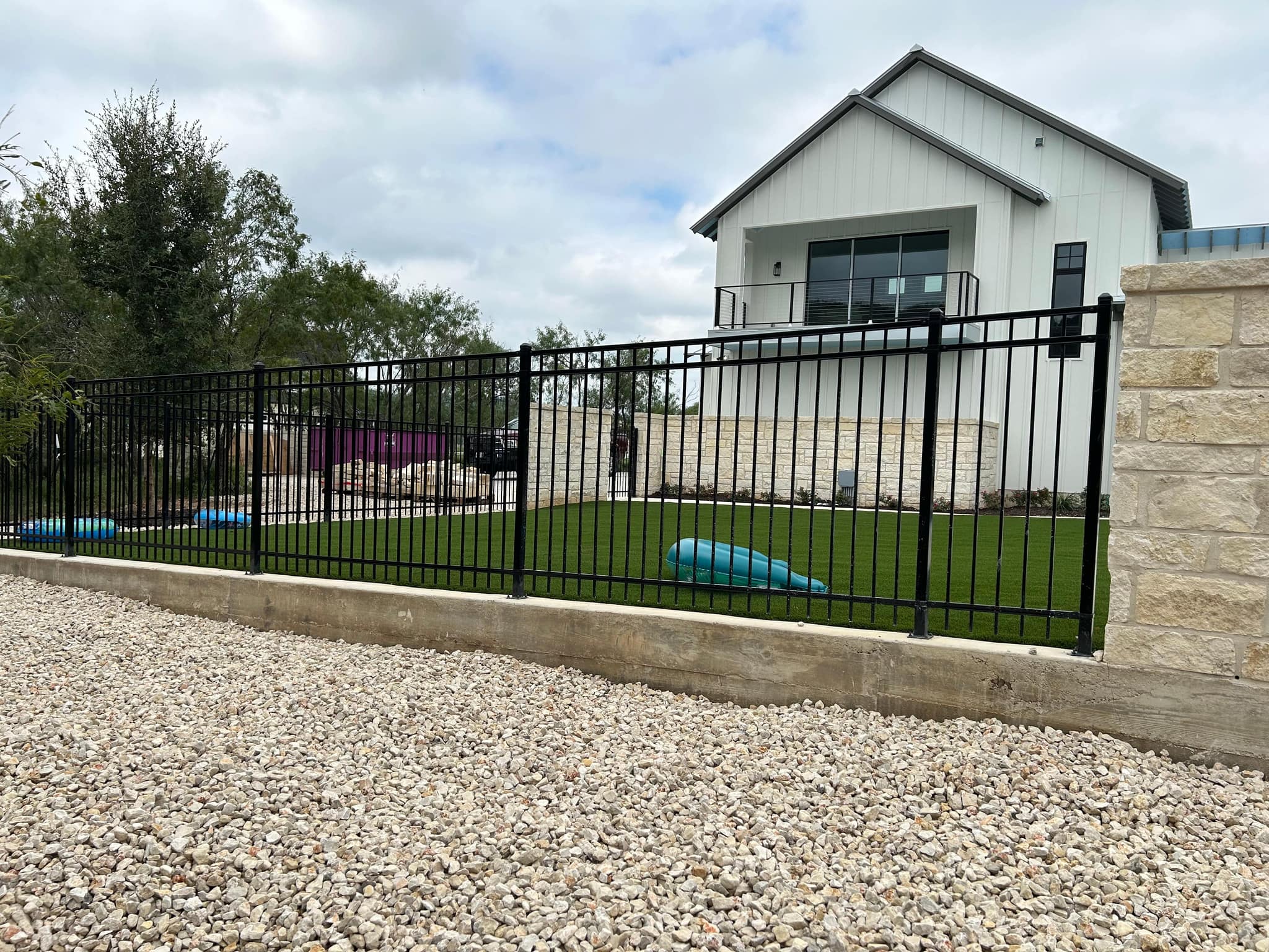Black iron fence set on a low wall in front of a white farmhouse