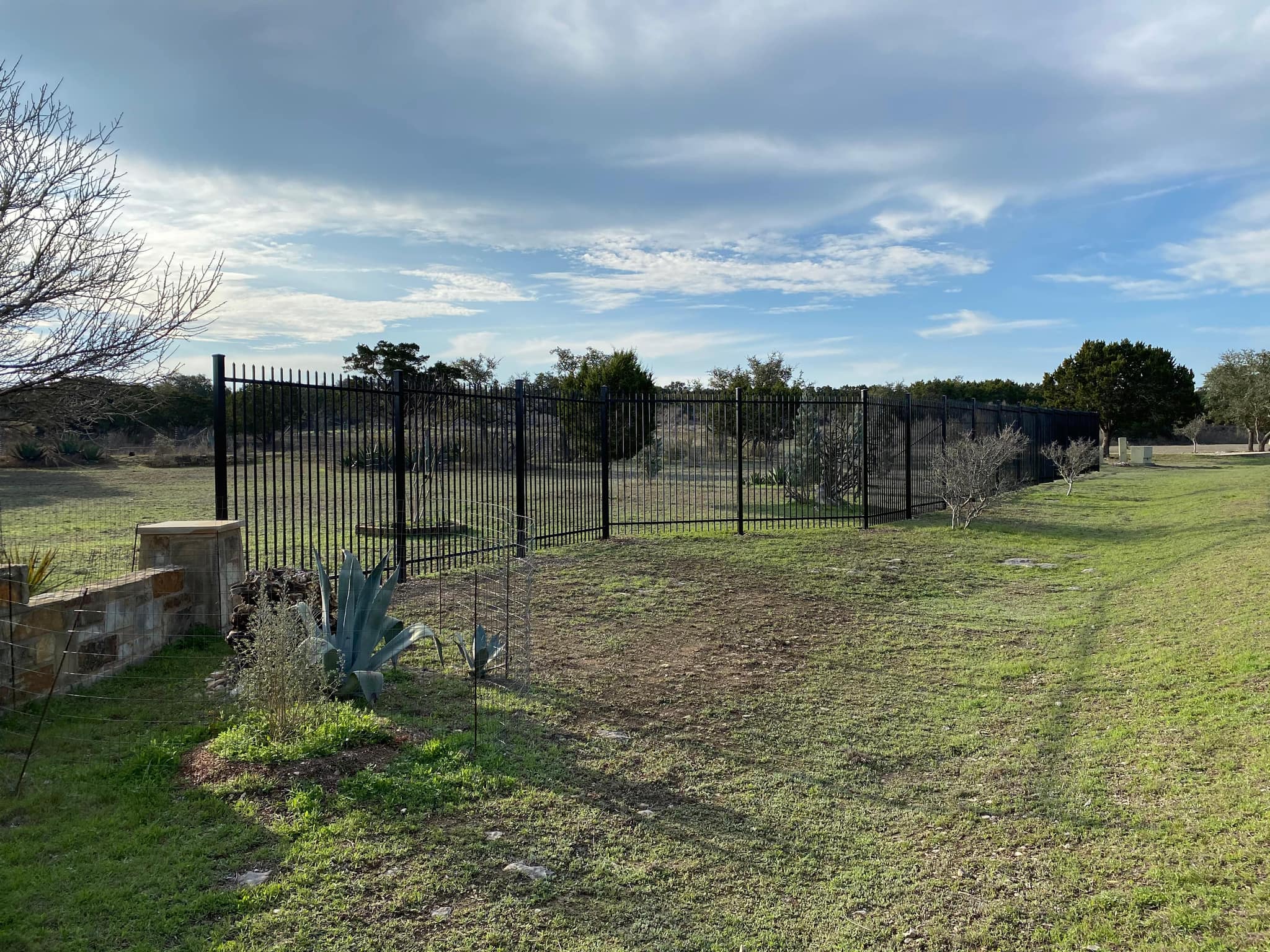 Black iron fence running along open land from a stone column