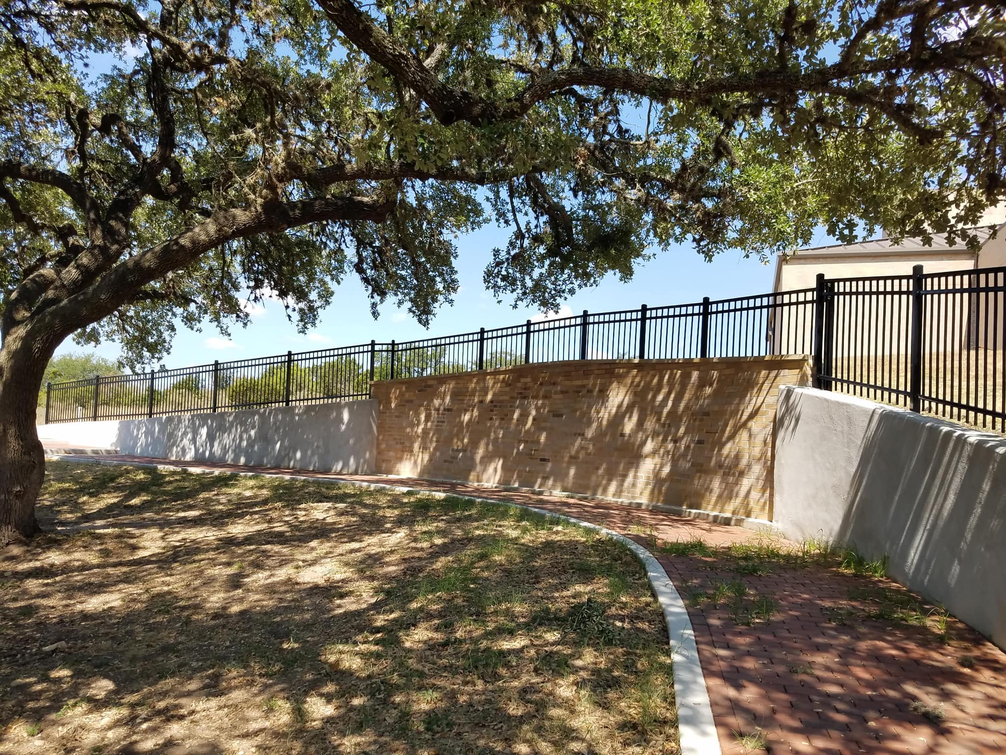 Black iron fence along the top of a curved retaining wall under an oak