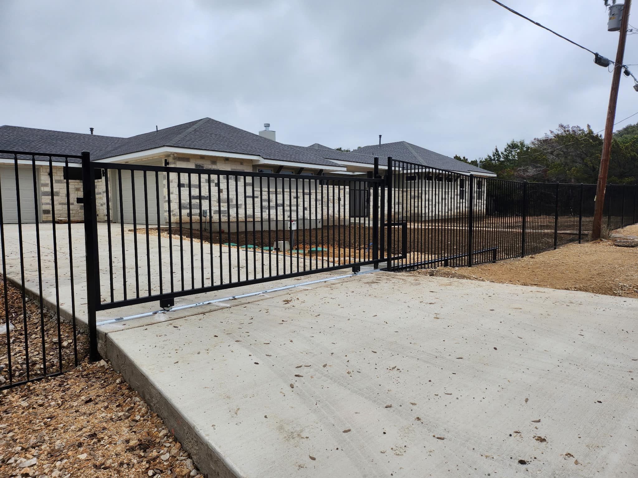 Black iron slide gate on a track across a concrete drive
