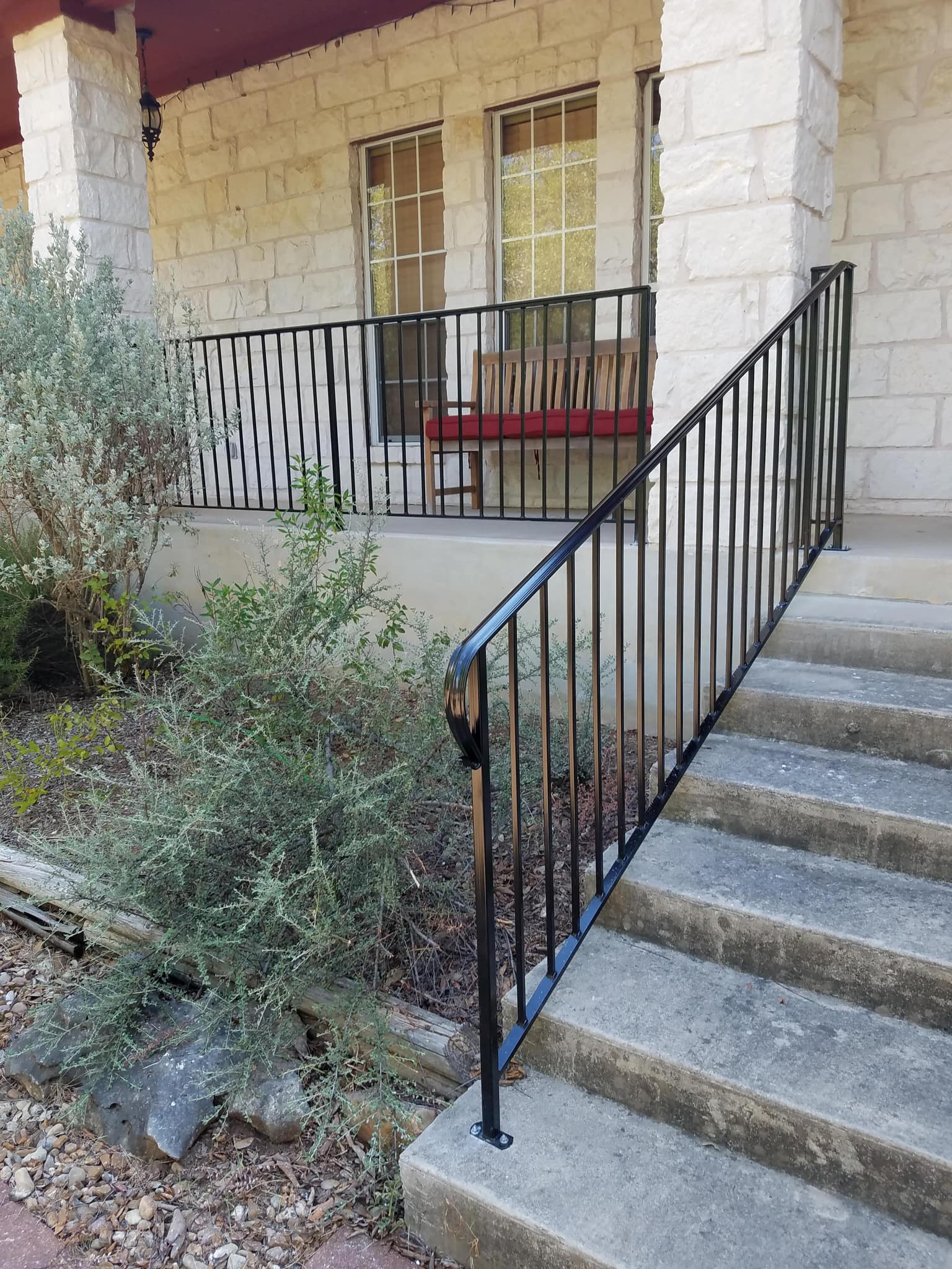 Black iron handrail up concrete steps to a stone porch, with matching porch railing