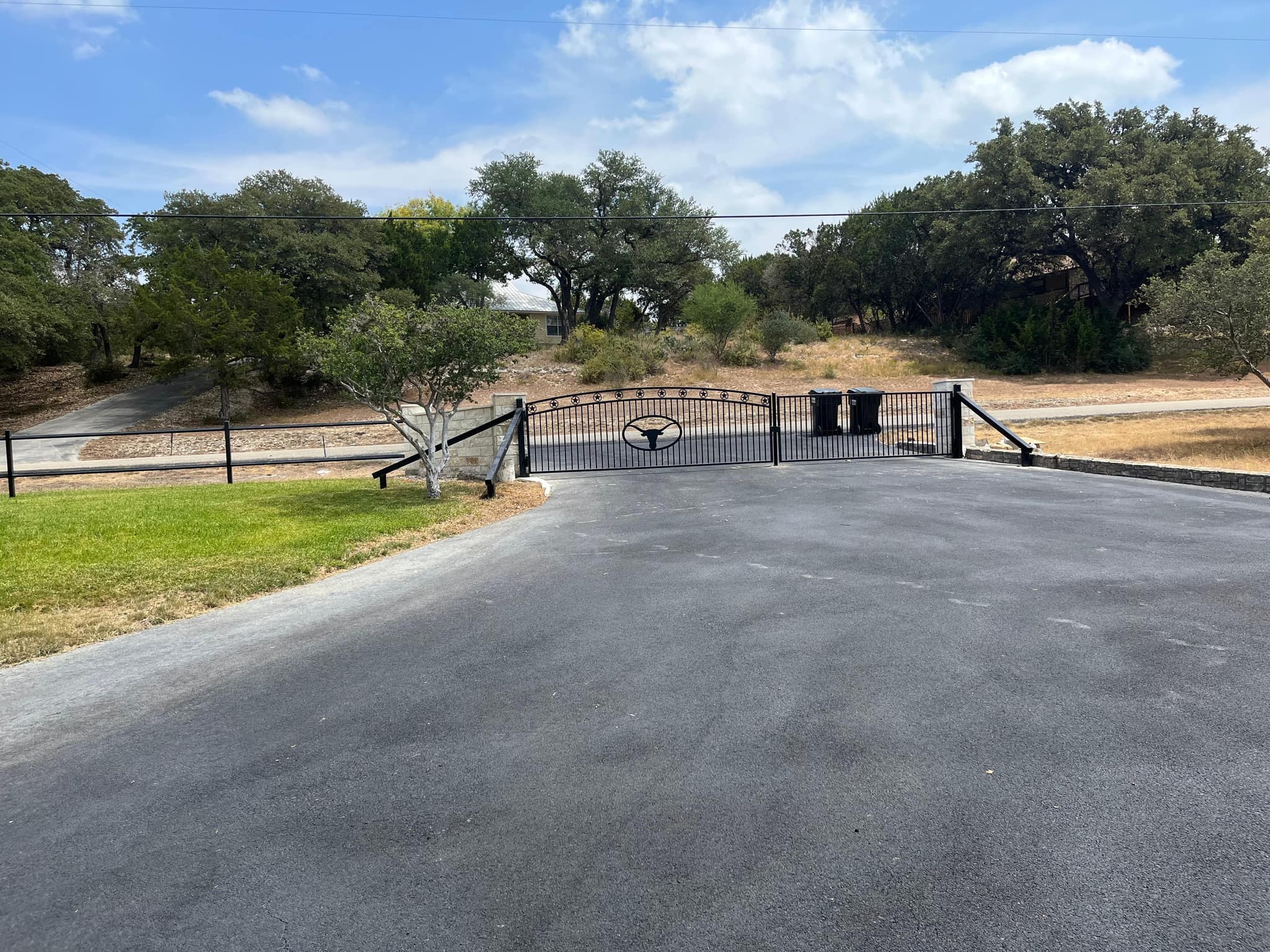 Arched iron driveway gate with a longhorn medallion across an asphalt drive