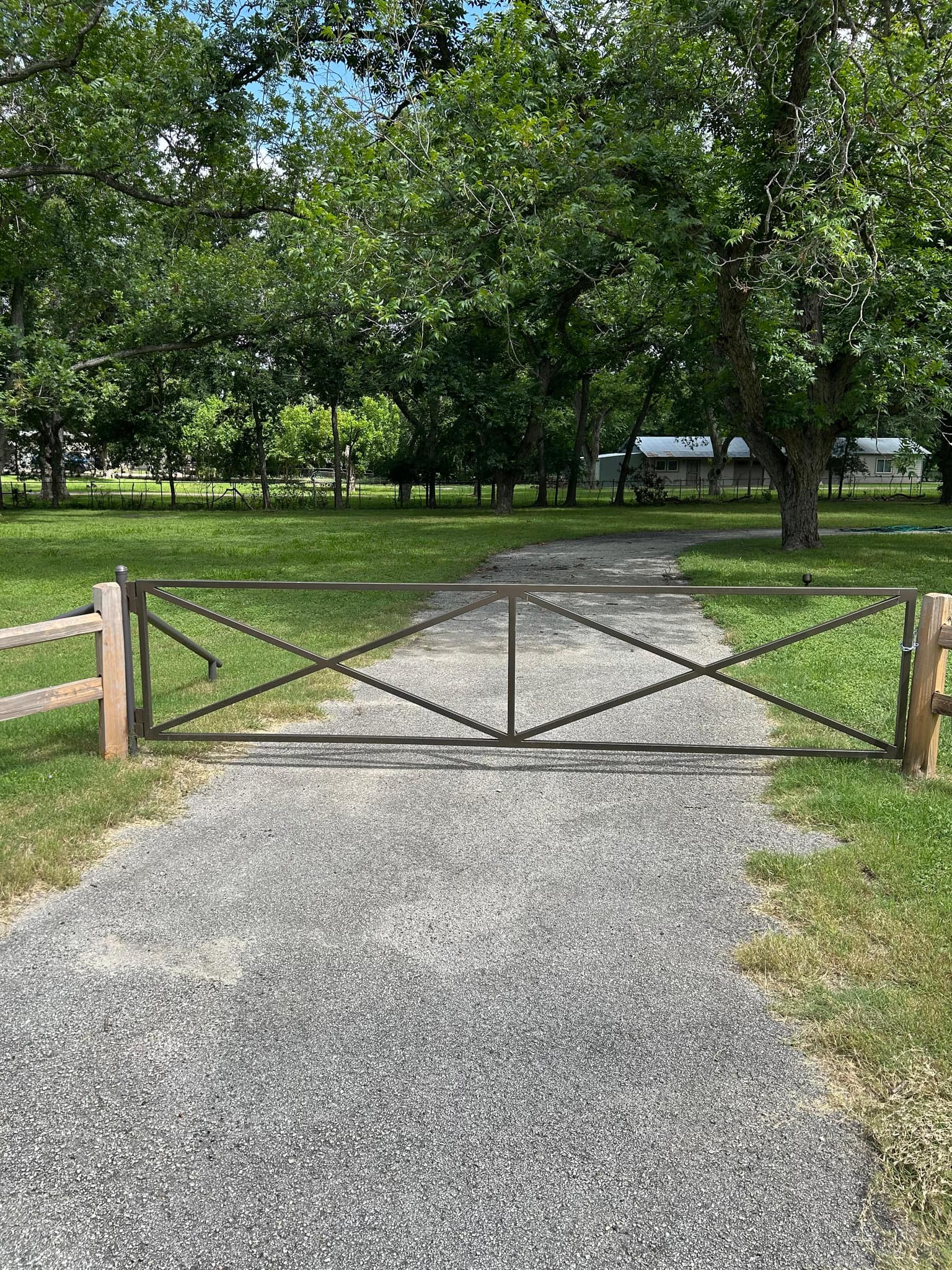 Steel pipe gate with an X brace between cedar posts across a gravel drive