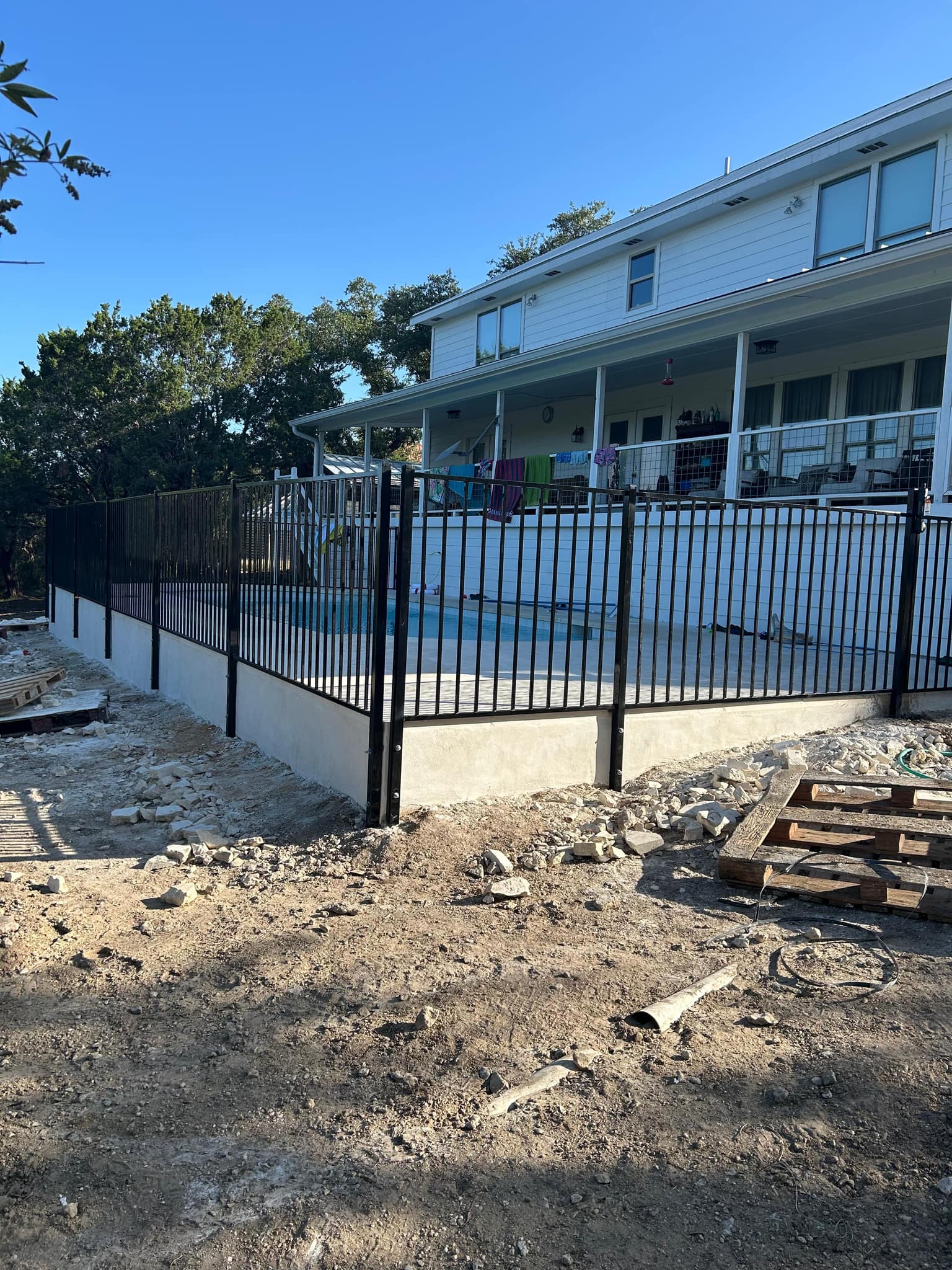 Black iron fence along the raised wall of a pool beside a two-story house