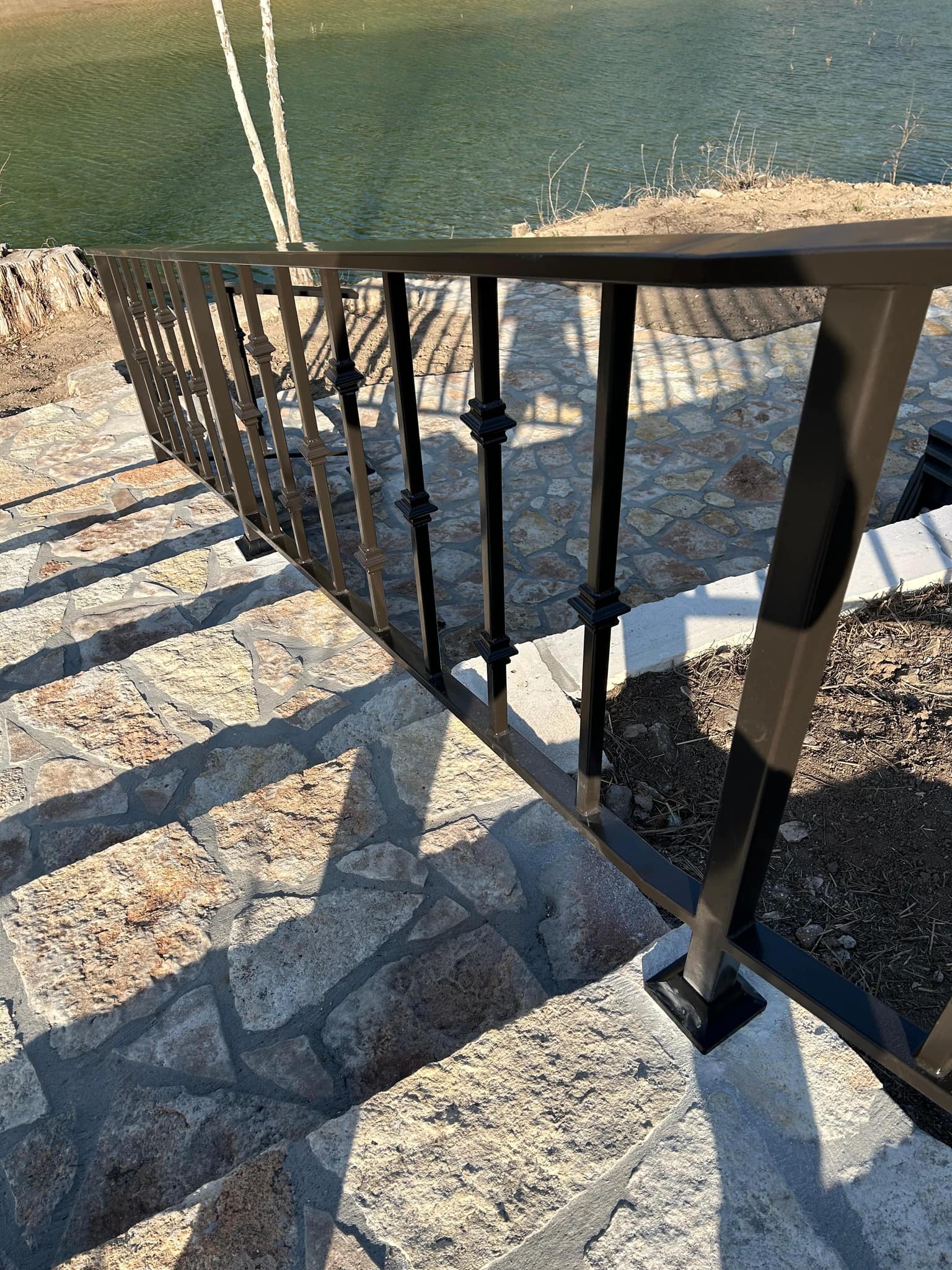 Black iron railing on base plates down limestone steps toward the water