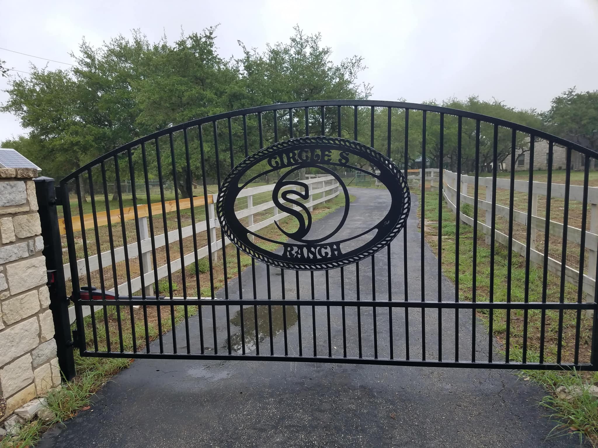 Arched iron driveway gate with an oval ranch-name and brand medallion