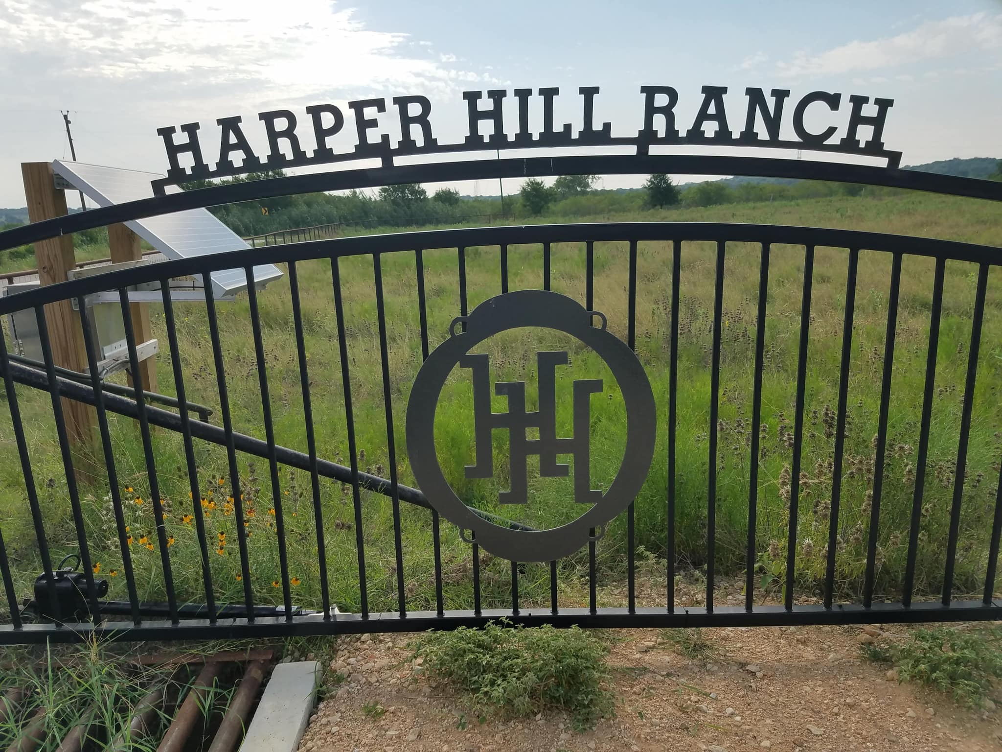 Iron ranch-name arch above a driveway gate with a round initial brand
