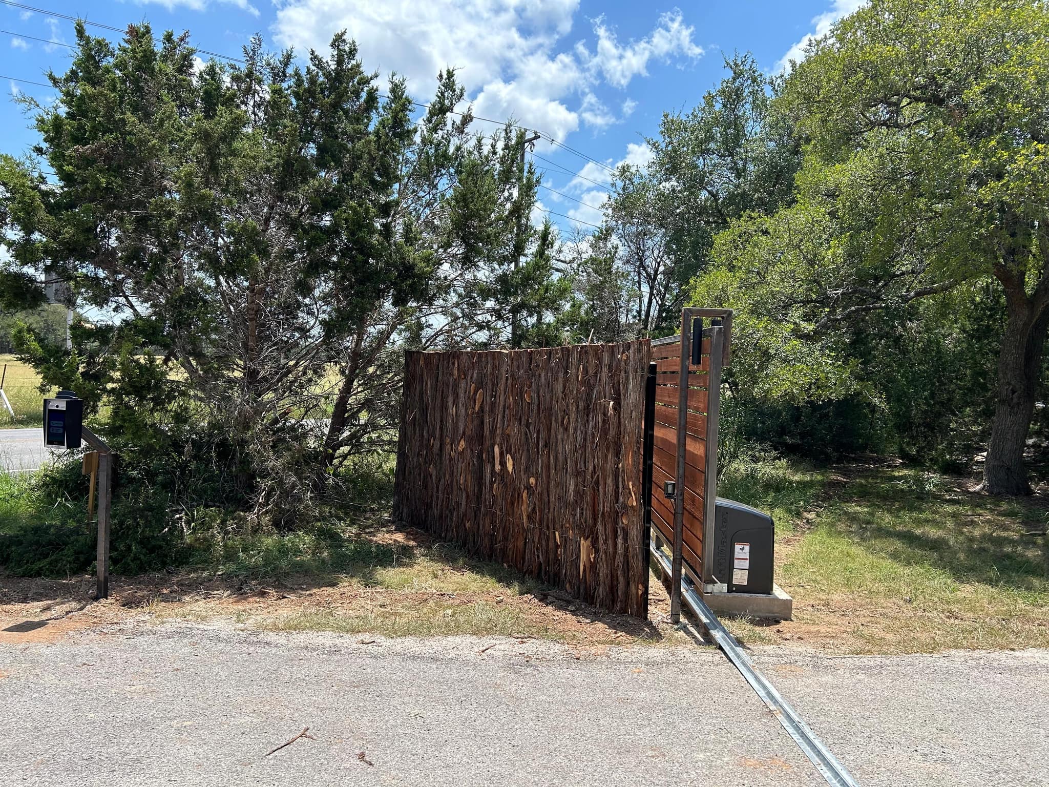 Rough-sawn cedar slide gate with an opener at the end of a drive