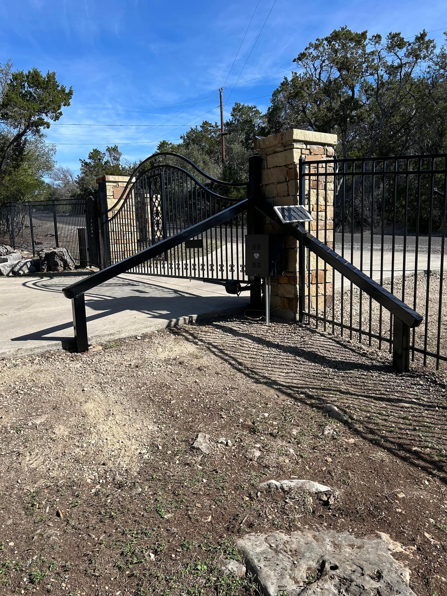 The same arched gate from inside: opener arm, control box and solar panel on the gate post, with steel guard rails