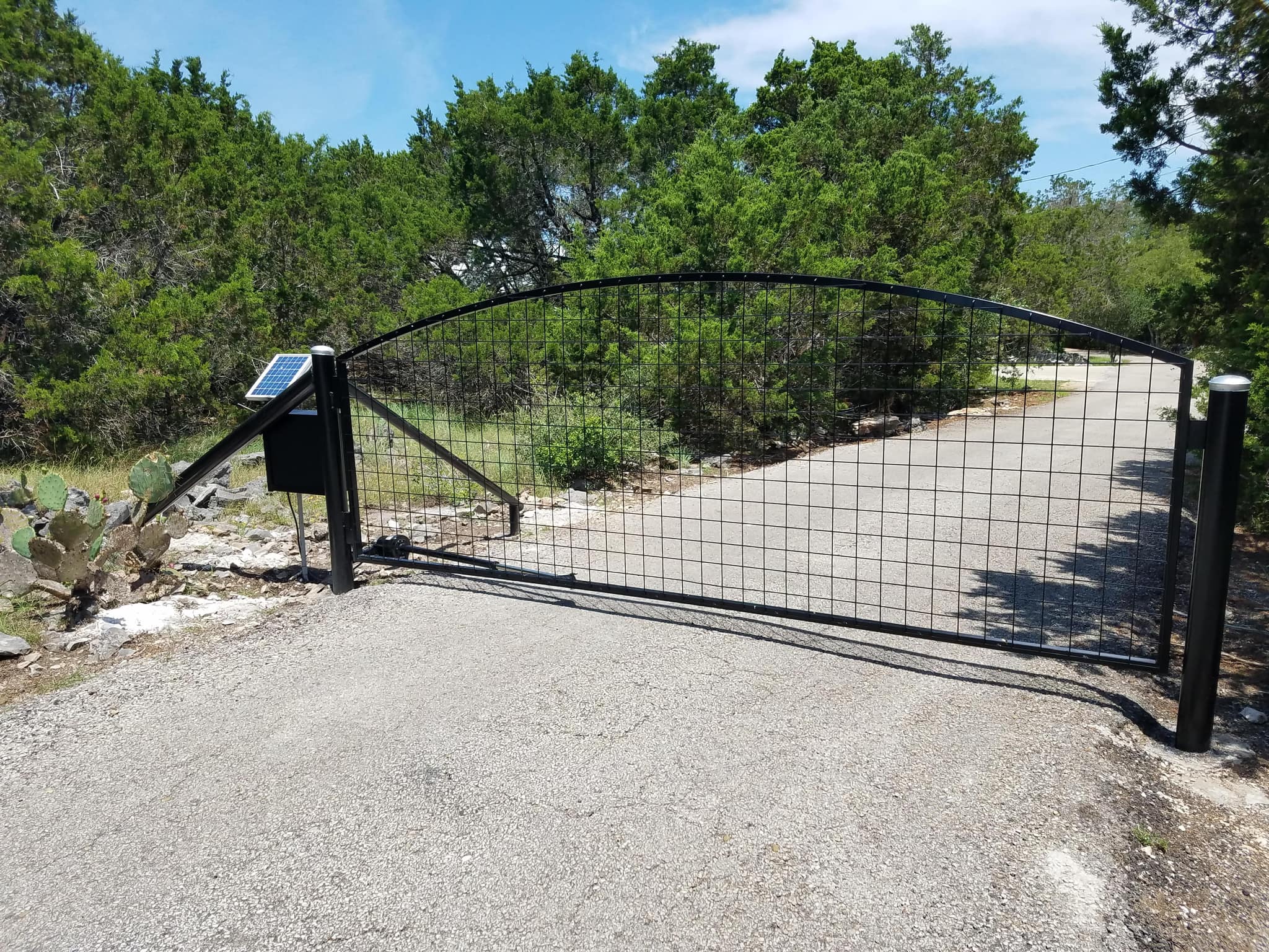 Arched black wire-panel driveway gate with a solar panel and opener