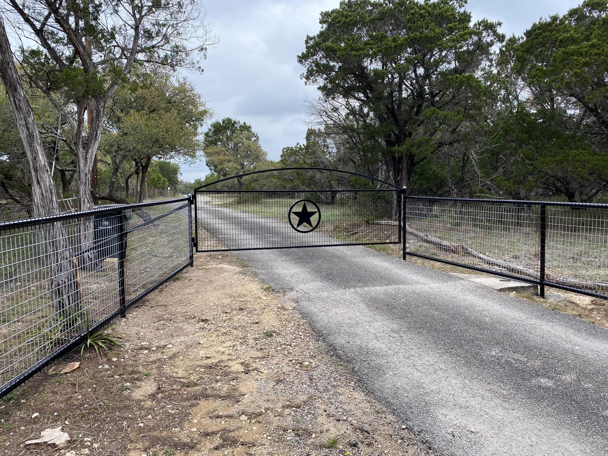 Arched driveway gate with a star, in a black wire panel fence