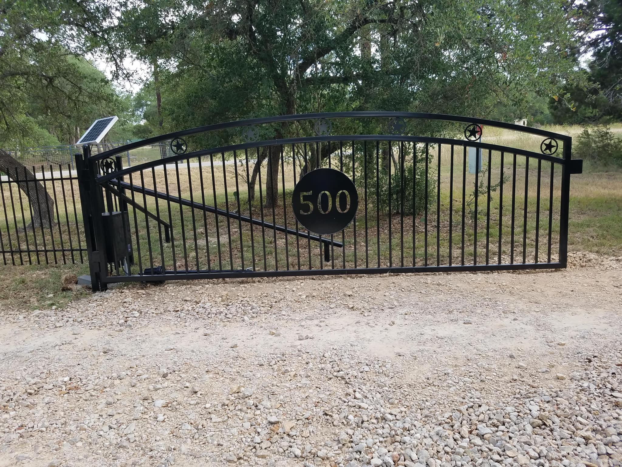 Arched iron driveway gate with stars and a round house-number plate, with a solar-powered opener