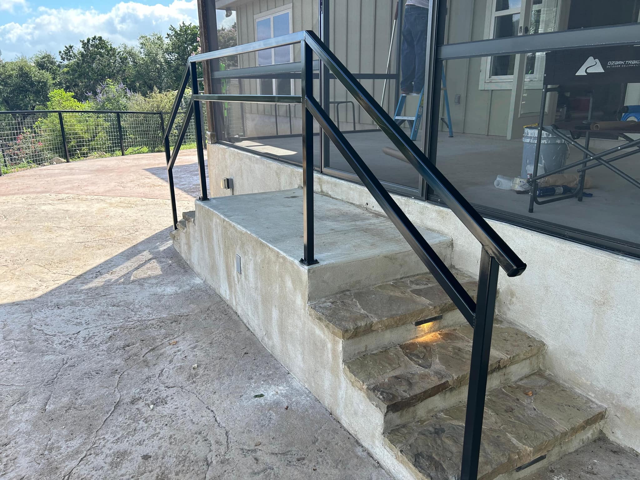 Black square-tube handrail up stone steps to a porch