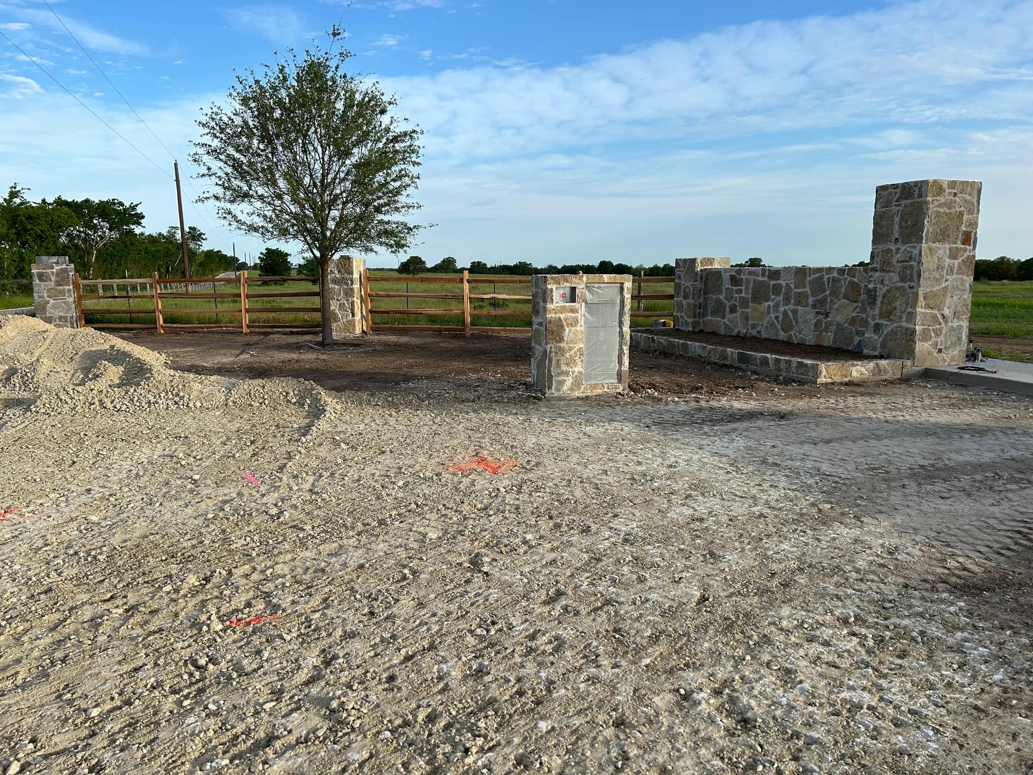 Stone columns and a stone wall with a three-rail wood ranch fence along open land