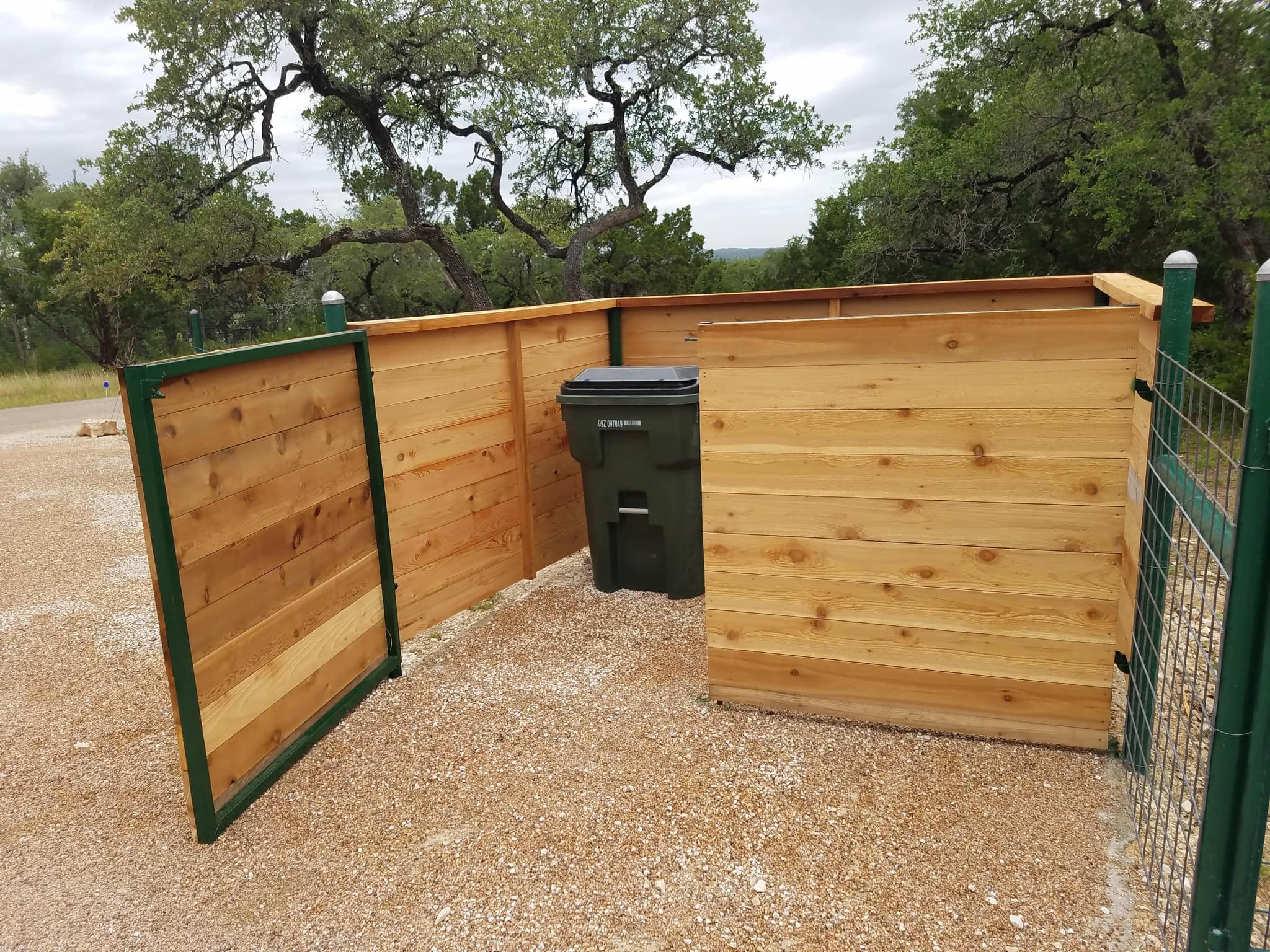Horizontal cedar enclosure around trash bins, with a green steel-framed cedar gate