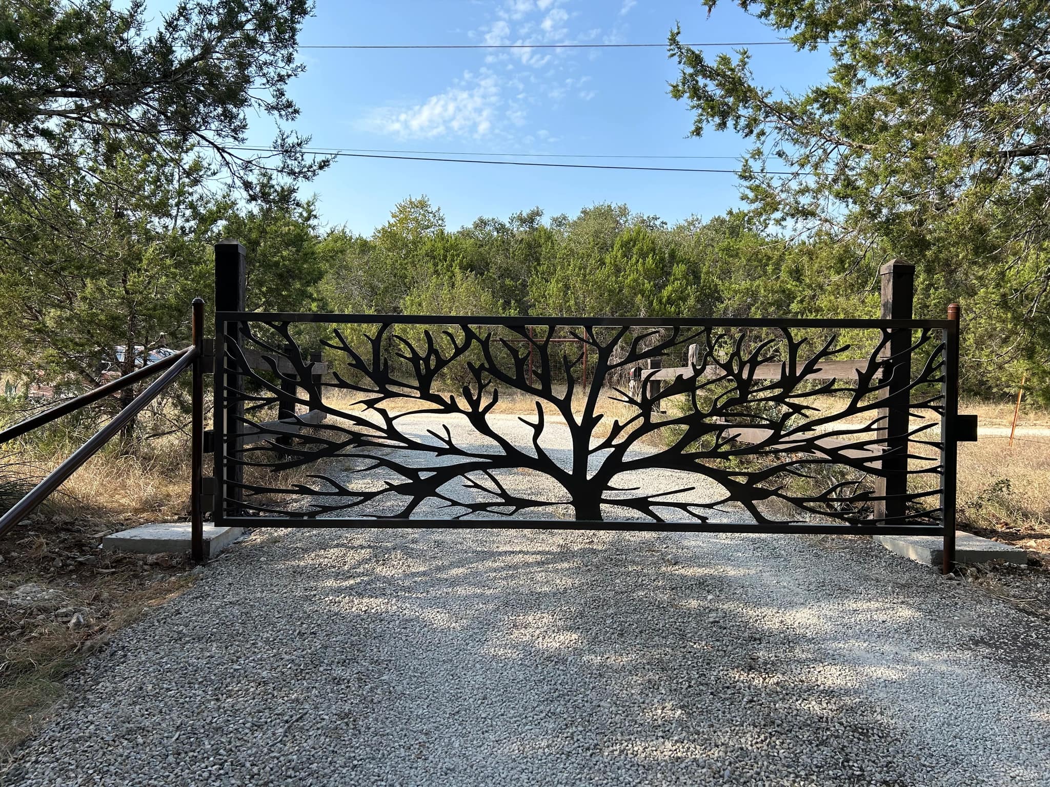 Cut-steel driveway gate with a spreading tree design between wood posts