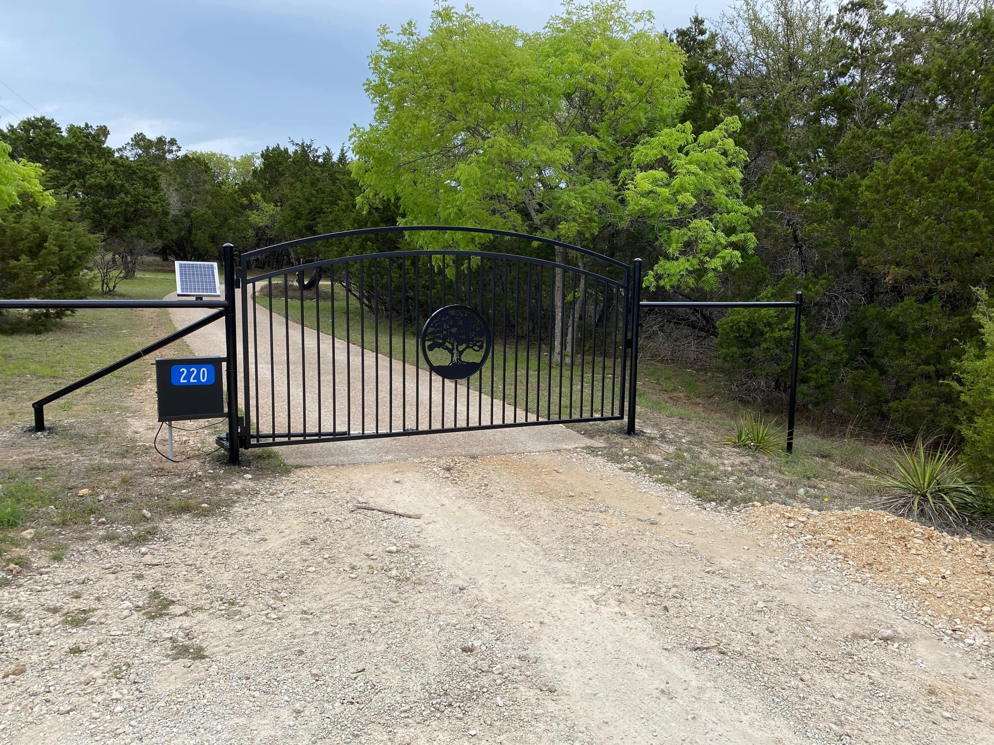 Arched iron driveway gate with a tree medallion, solar panel and keypad