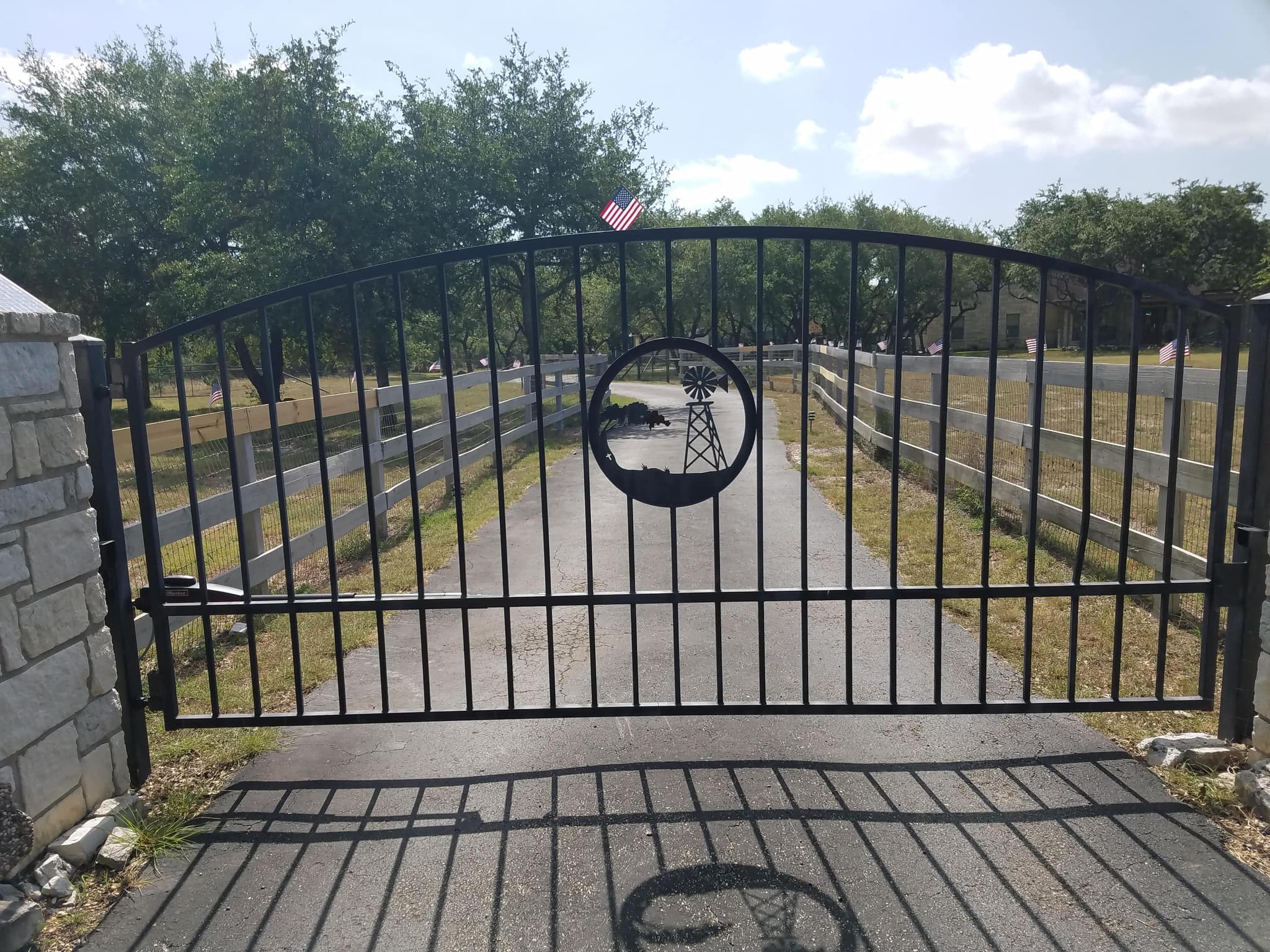 Arched iron driveway gate with a cut-steel windmill and cattle medallion