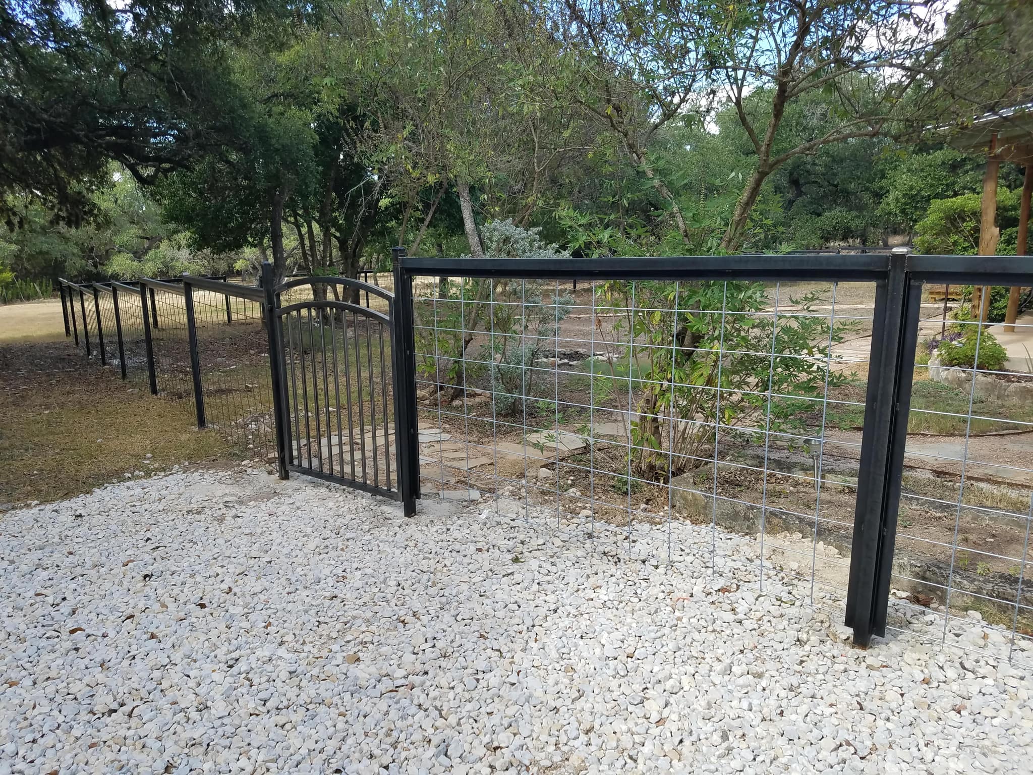 Black steel-framed welded-wire fence with an arched iron walk gate over white gravel